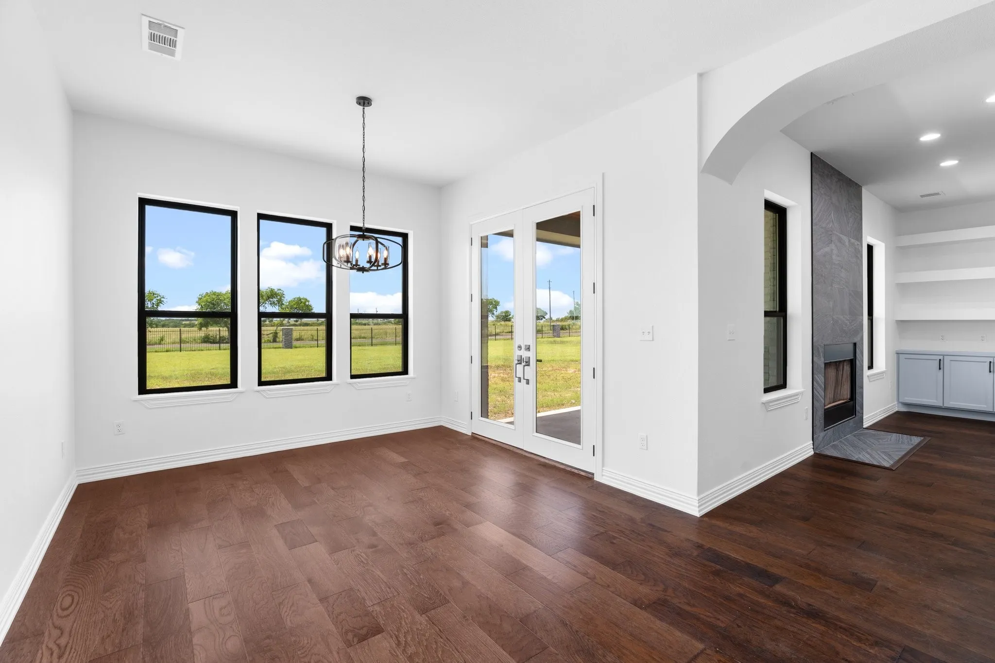 Empty room featuring dark wood-style flooring, arched walkways, a chandelier, recessed lighting, and built in features