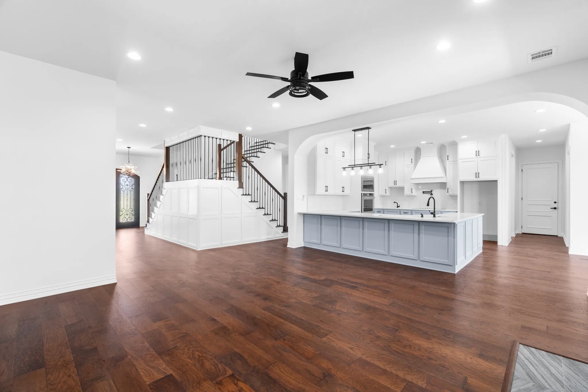 Unfurnished living room featuring arched walkways, dark wood-type flooring, stairway, a ceiling fan, and recessed lighting