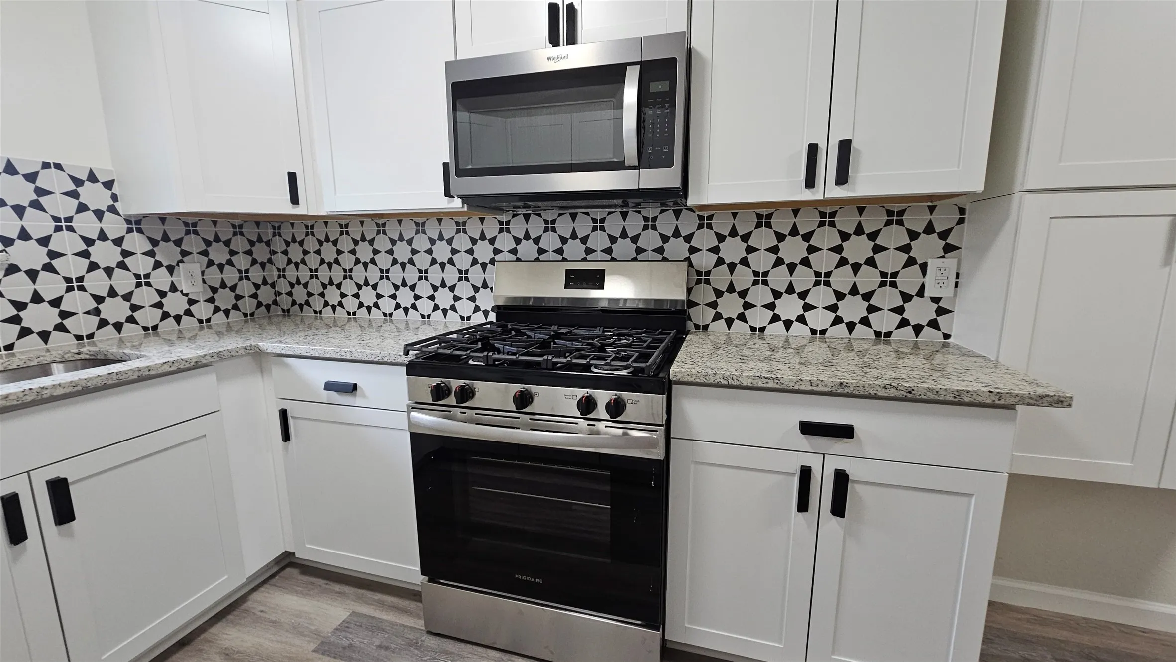 Kitchen with stainless steel appliances, white cabinetry, light wood-type flooring, and backsplash