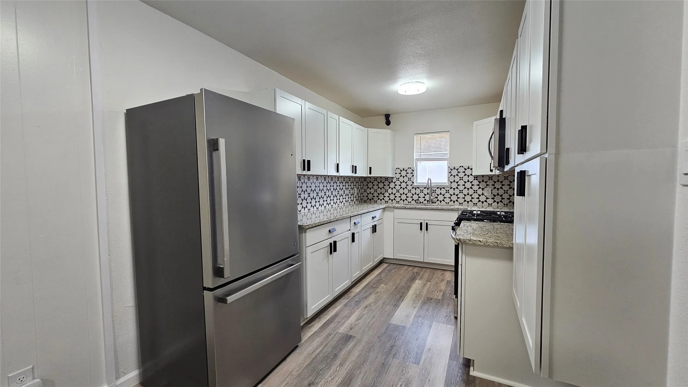 Kitchen with appliances with stainless steel finishes, wood finished floors, decorative backsplash, and white cabinetry