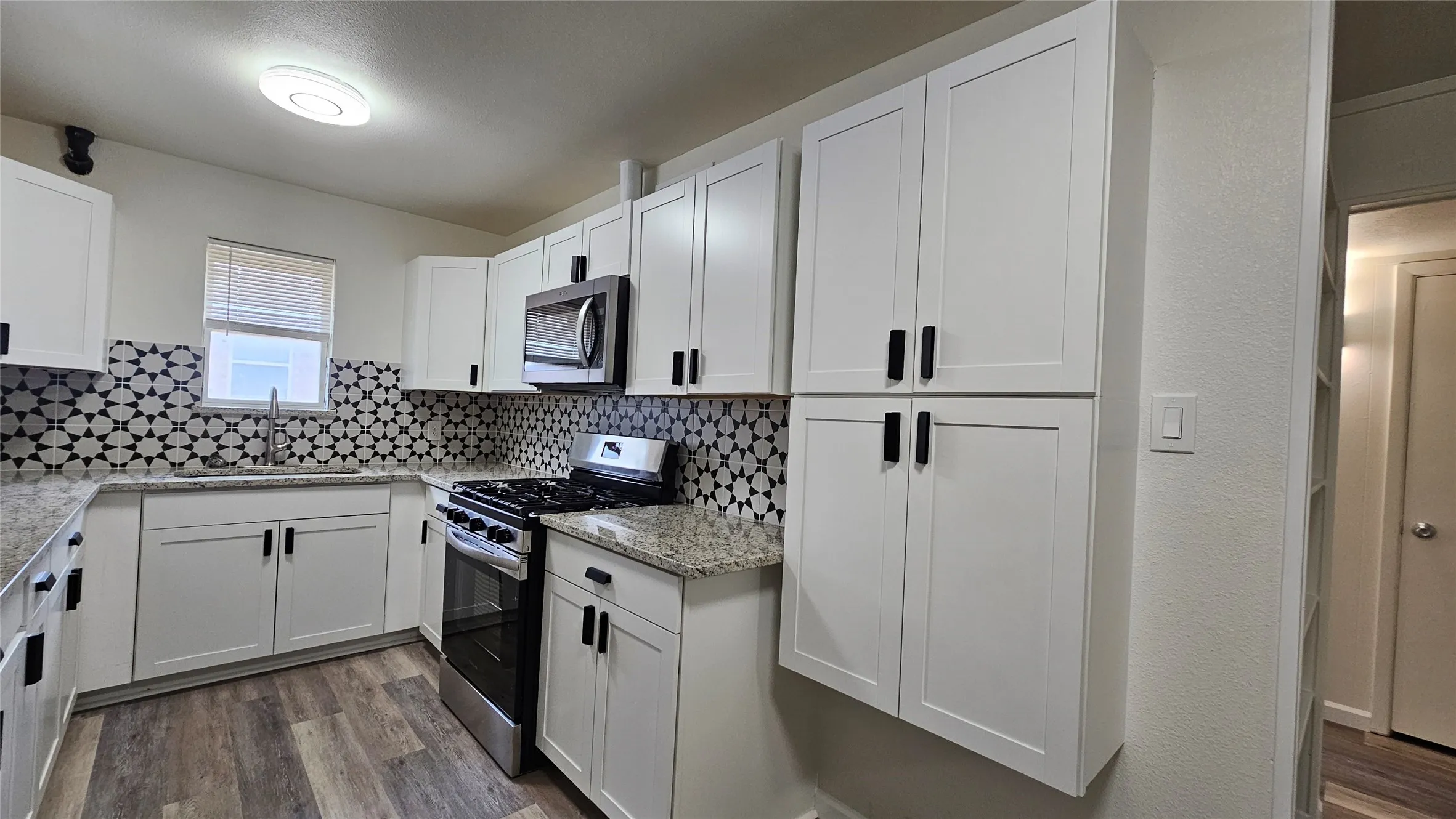 Kitchen featuring appliances with stainless steel finishes, wood finished floors, tasteful backsplash, and white cabinetry
