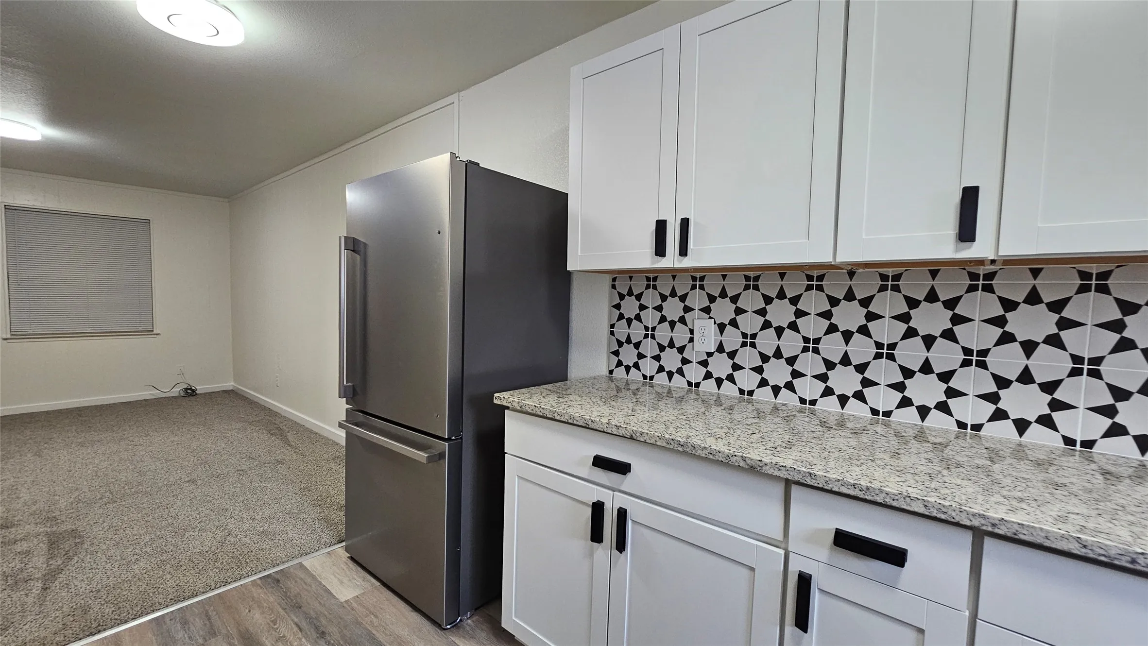 Kitchen featuring freestanding refrigerator, white cabinetry, decorative backsplash, light wood-style flooring, and light stone counters