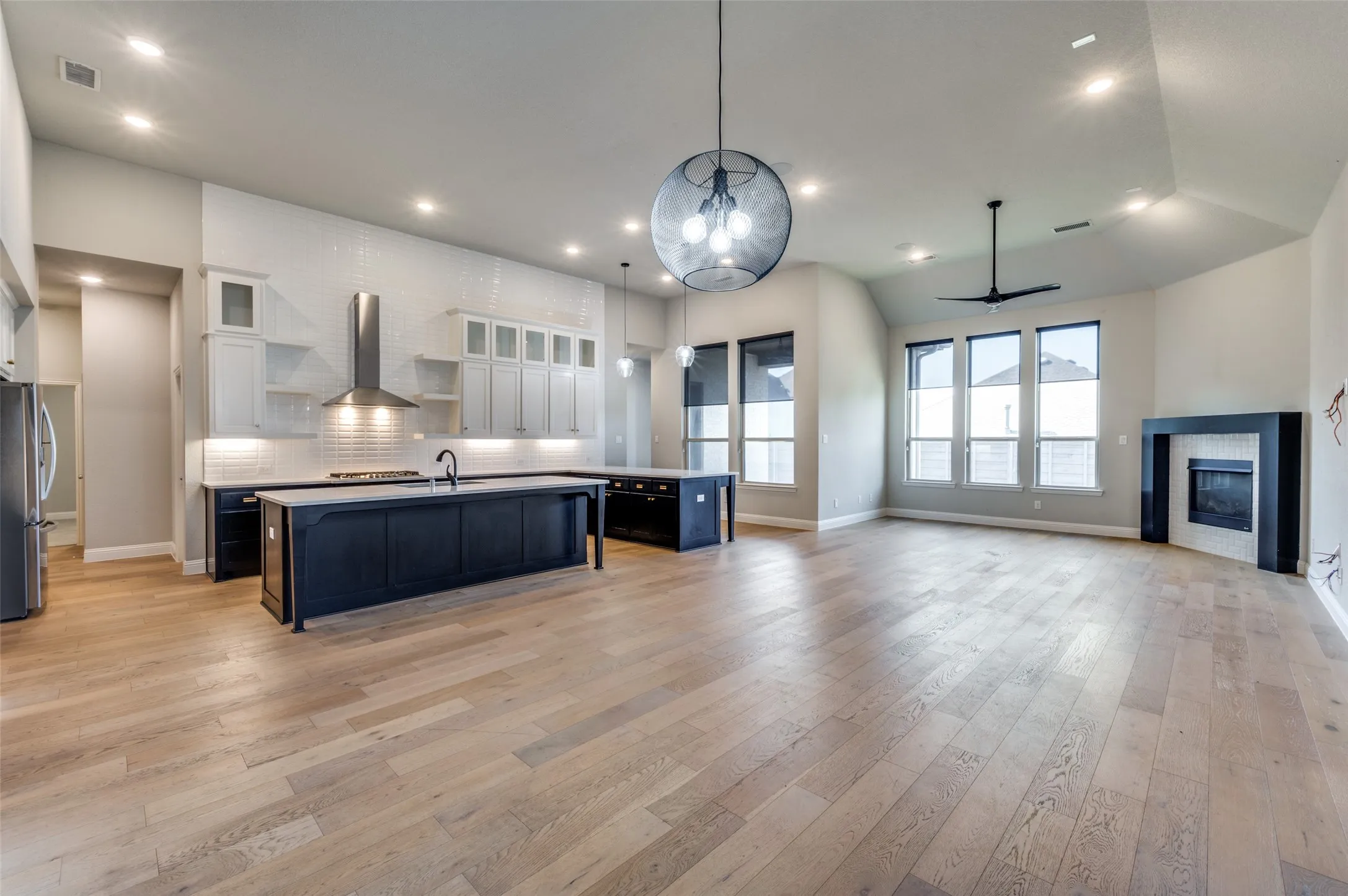 Kitchen with wall chimney range hood, an island with sink, a ceiling fan, light countertops, and white cabinets