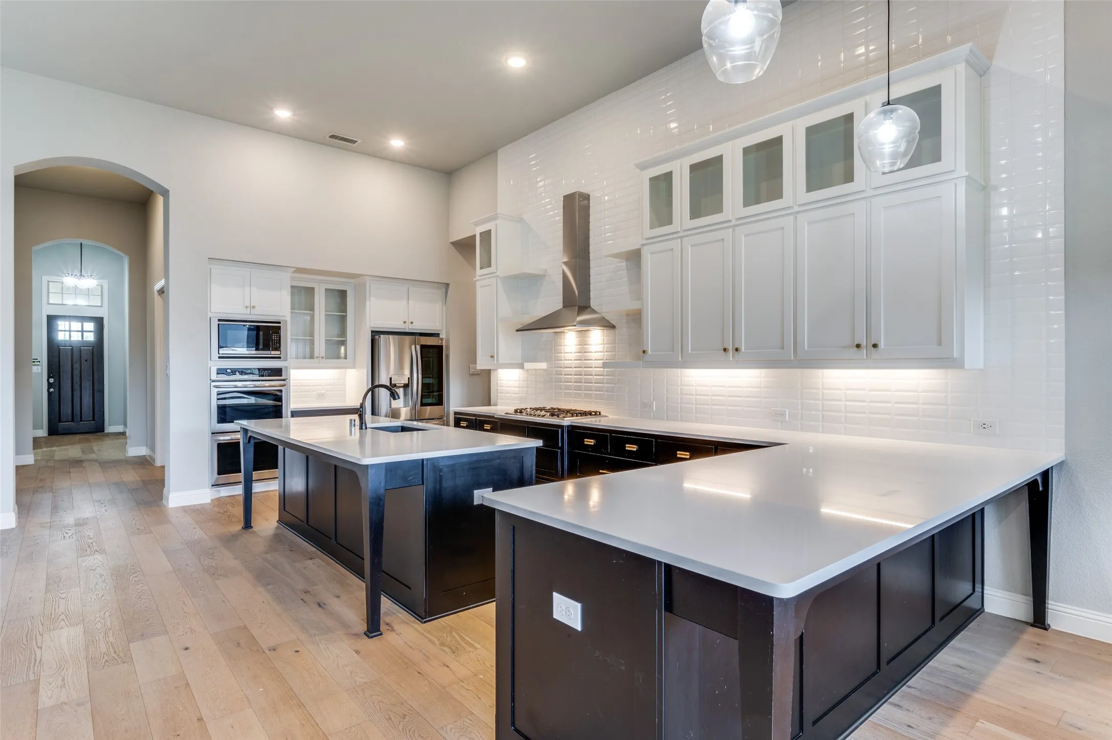 Kitchen featuring wall chimney range hood, appliances with stainless steel finishes, arched walkways, a breakfast bar, and light countertops