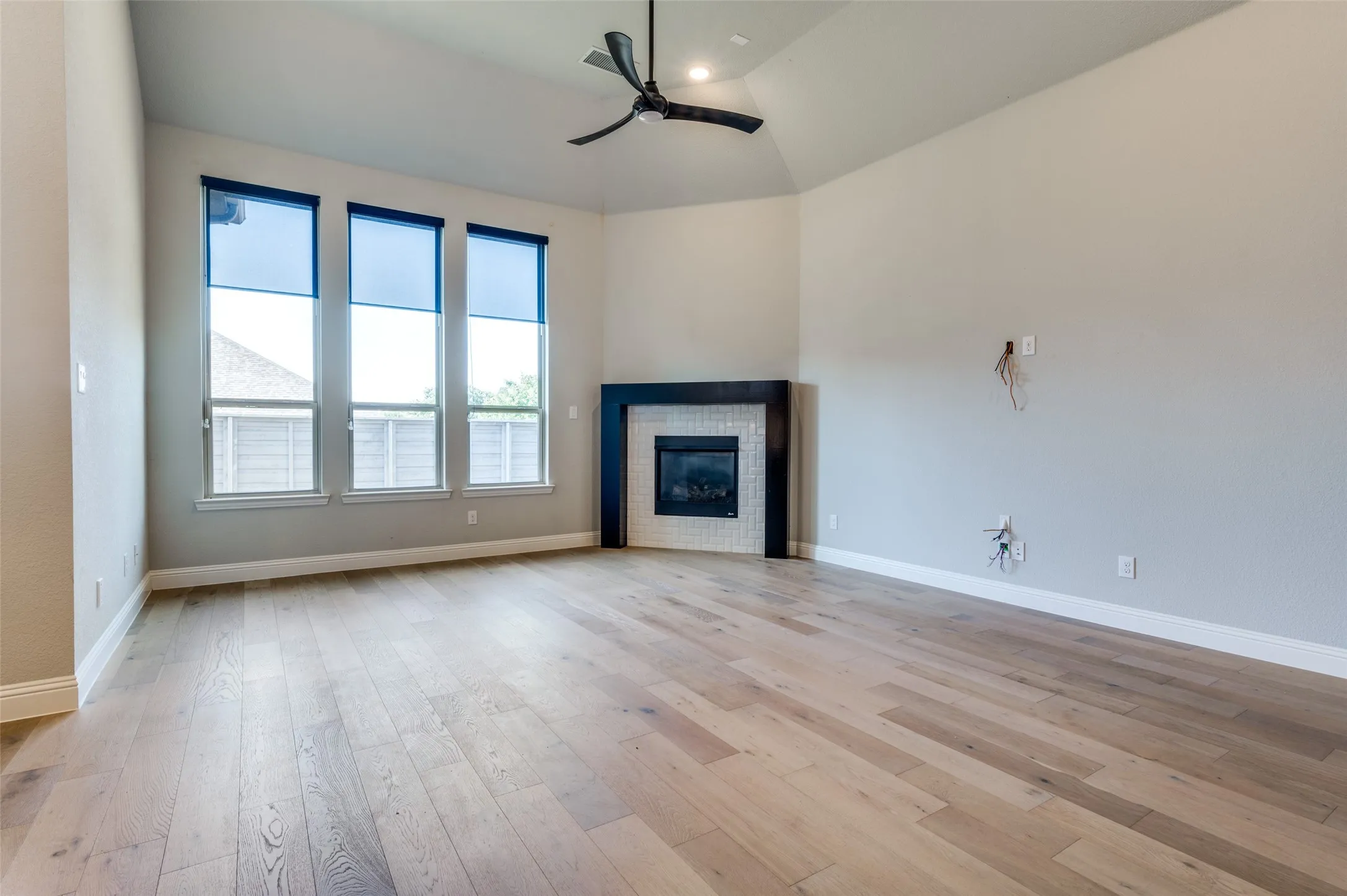 Living room featuring a ceiling fan, light wood finished floors, a fireplace, and high vaulted ceiling