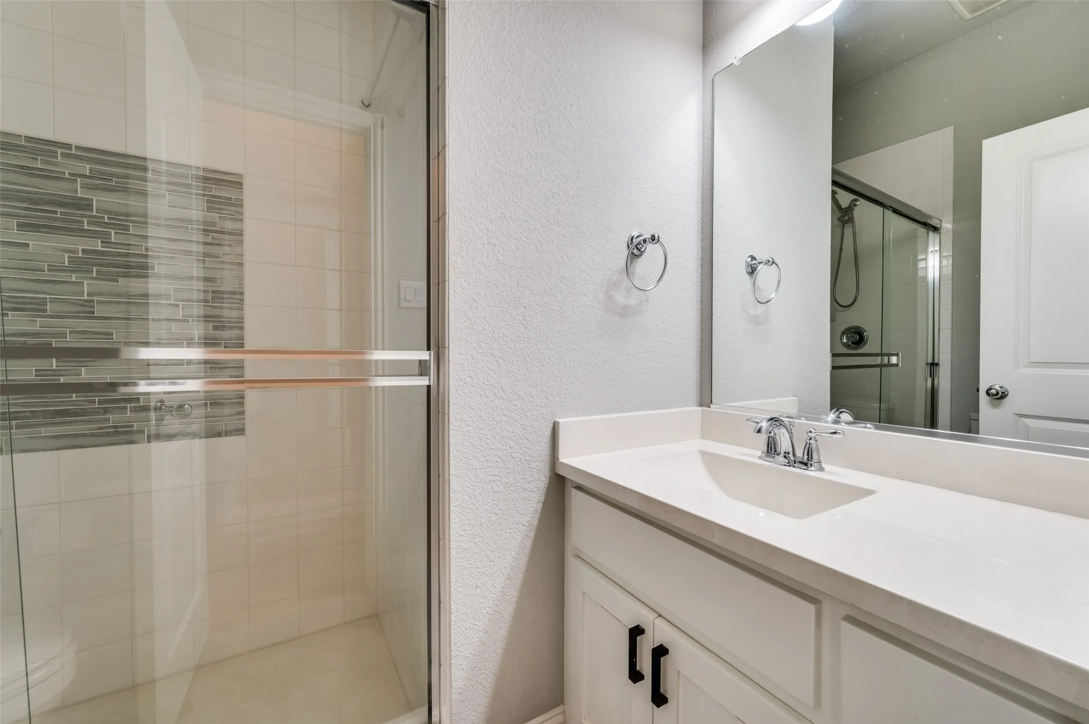 Bathroom with a stall shower, a textured wall, and vanity