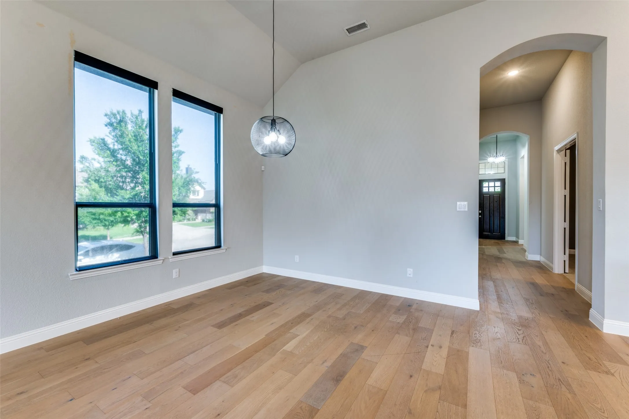 Dining area with arched walkways, light wood-style flooring, and lofted ceiling