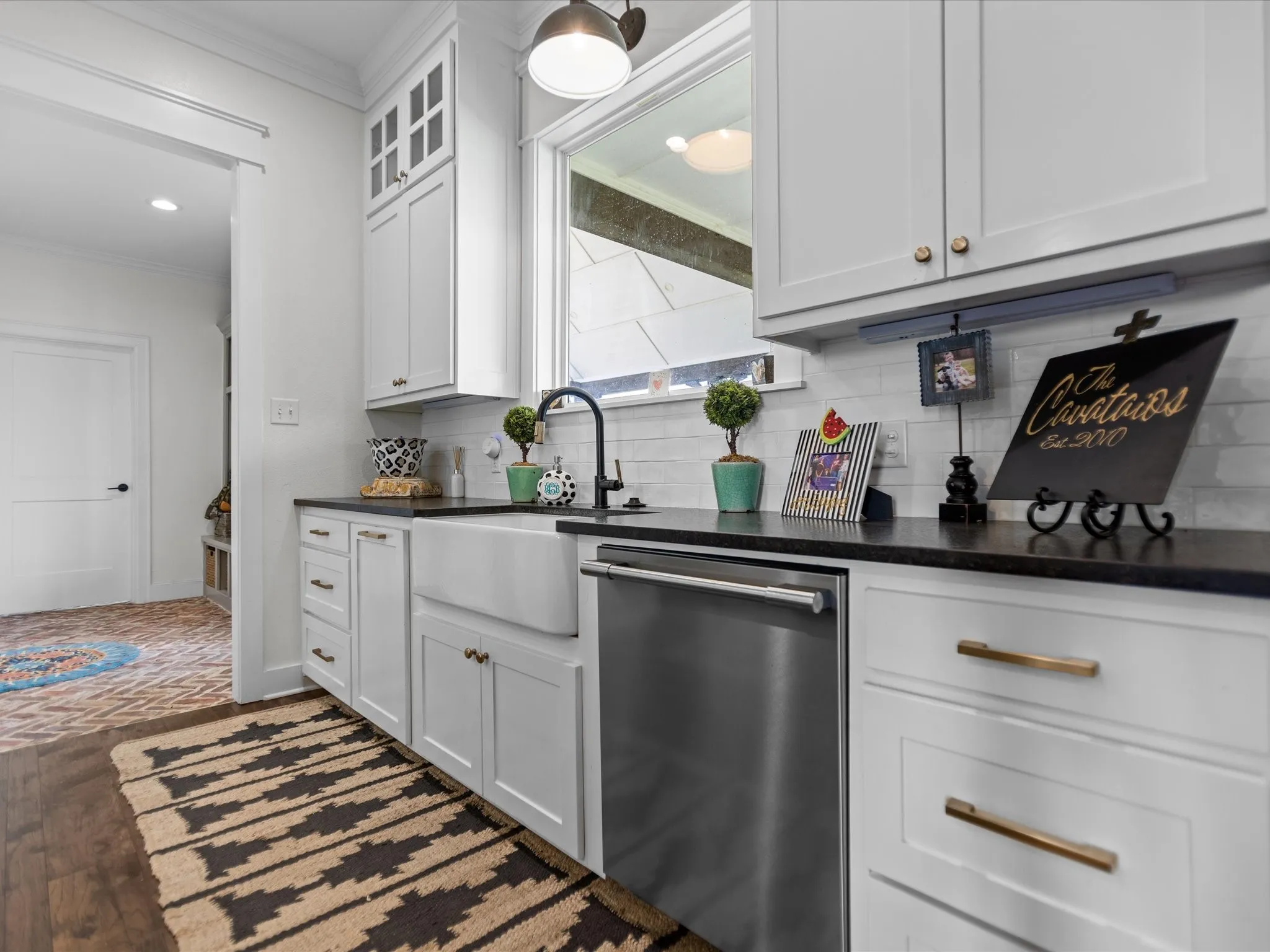 Kitchen featuring stainless steel dishwasher, ornamental molding, dark countertops, backsplash, and white cabinets