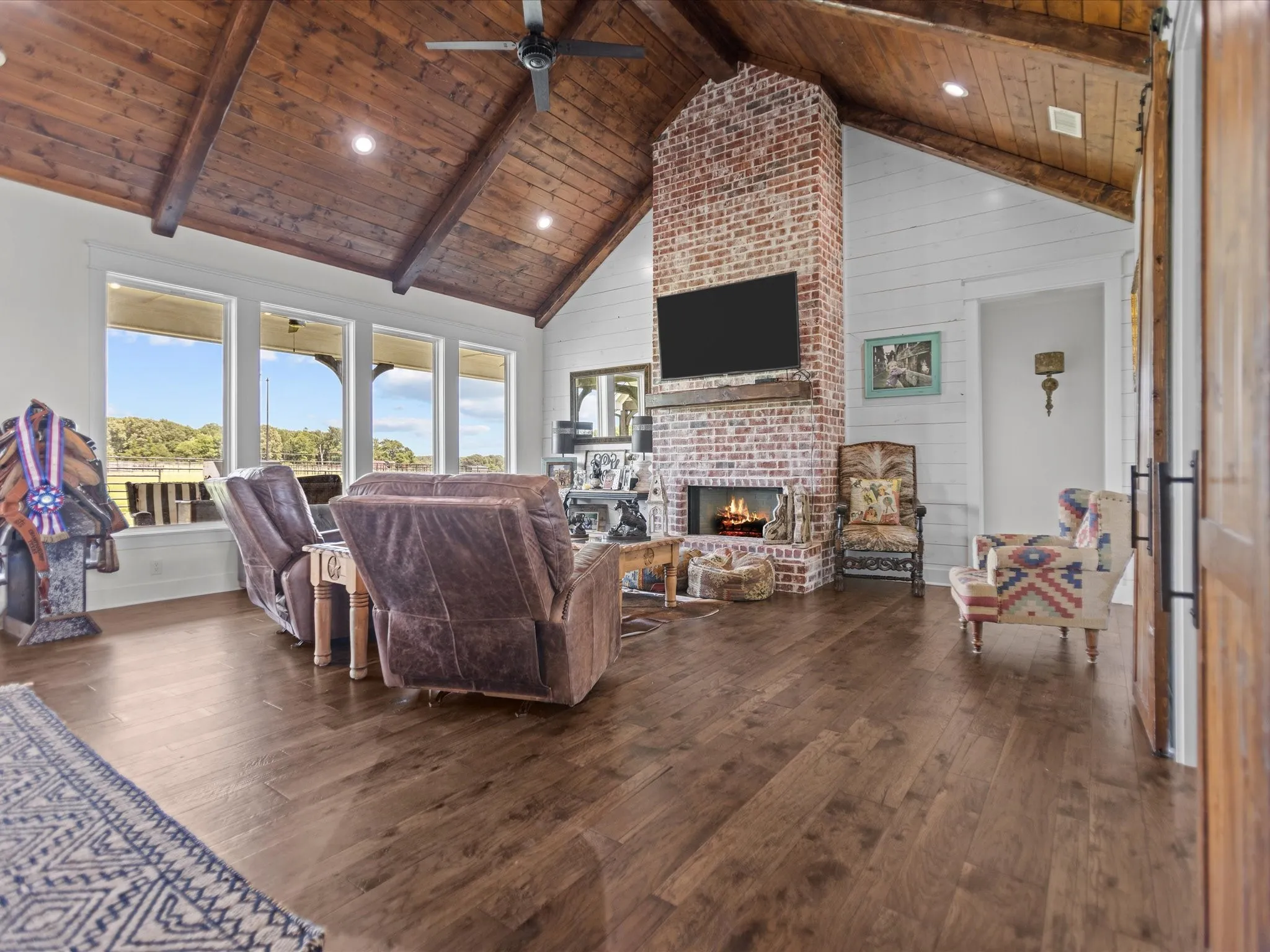 Living room featuring a wooden ceiling with exposed beams, high vaulted ceiling, dark wood-style floors, a brick fireplace, and a ceiling fan
