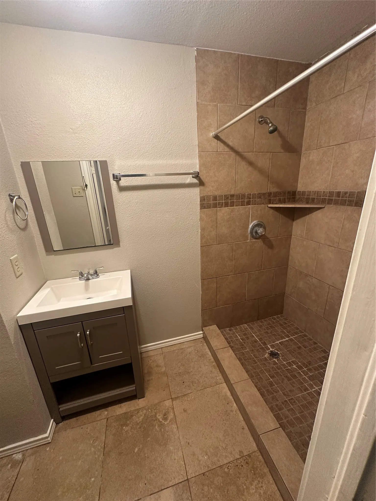 Full bath with a textured wall, vanity, a stall shower, a textured ceiling, and light tile patterned flooring