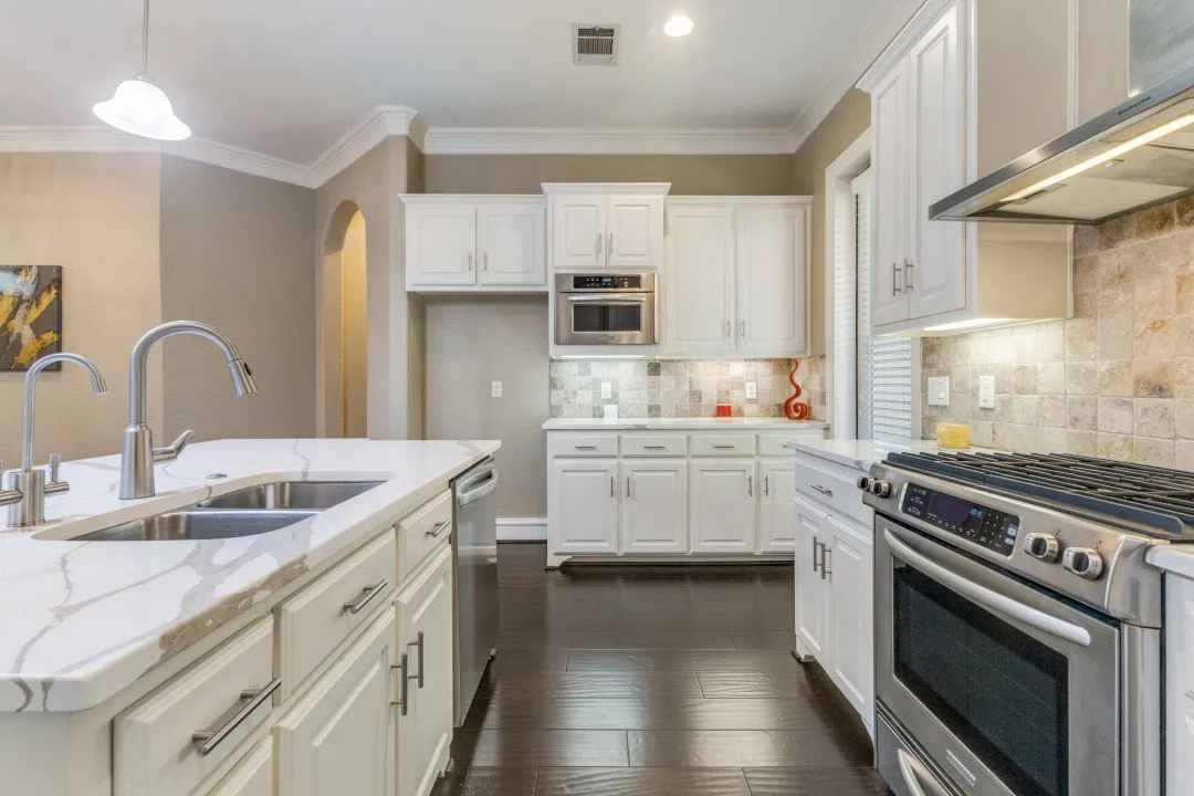 Kitchen featuring stainless steel appliances, wall chimney exhaust hood, decorative light fixtures, light stone countertops, and backsplash