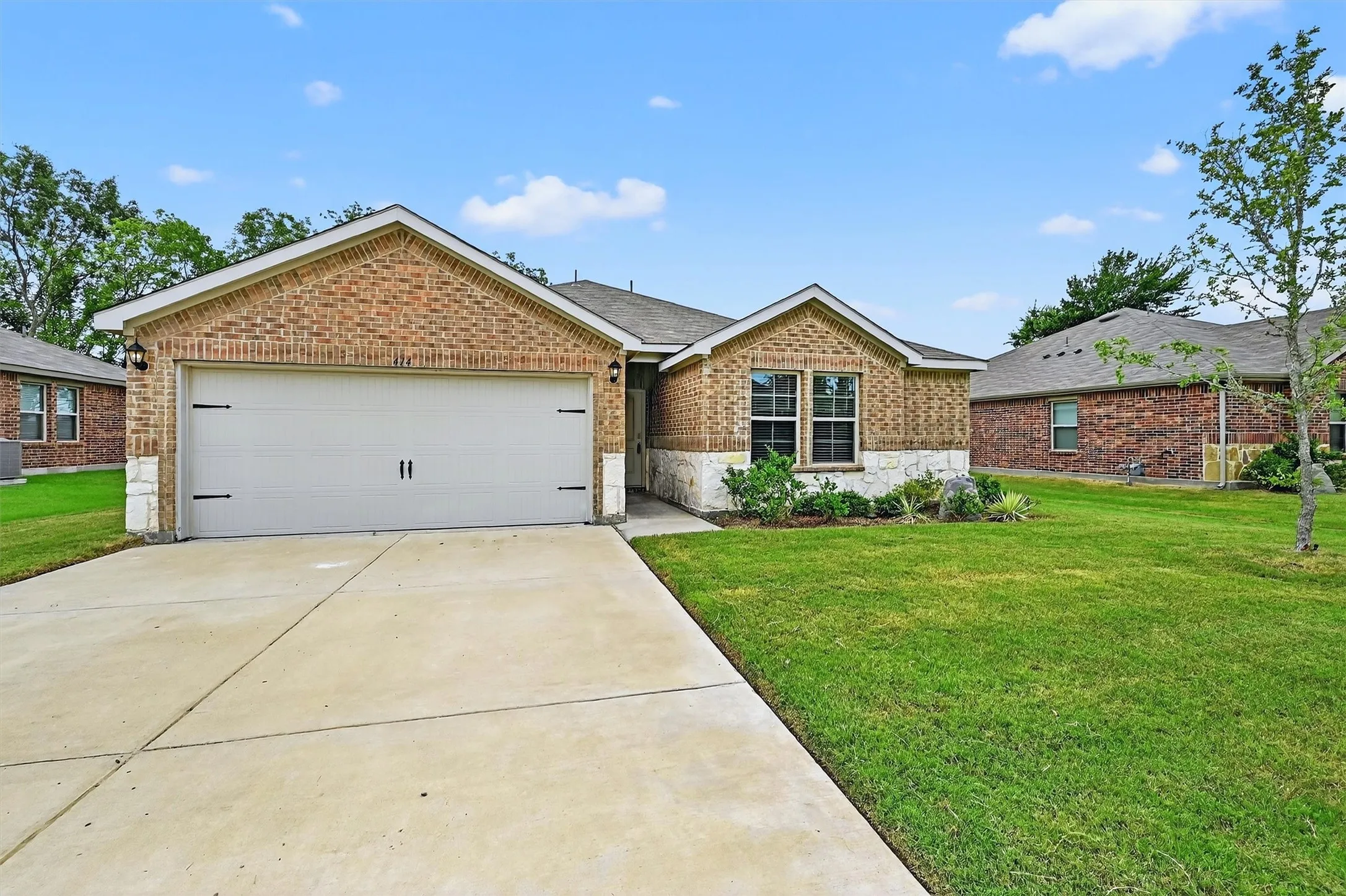 Ranch-style house with a garage, brick siding, driveway, a front lawn, and stone siding