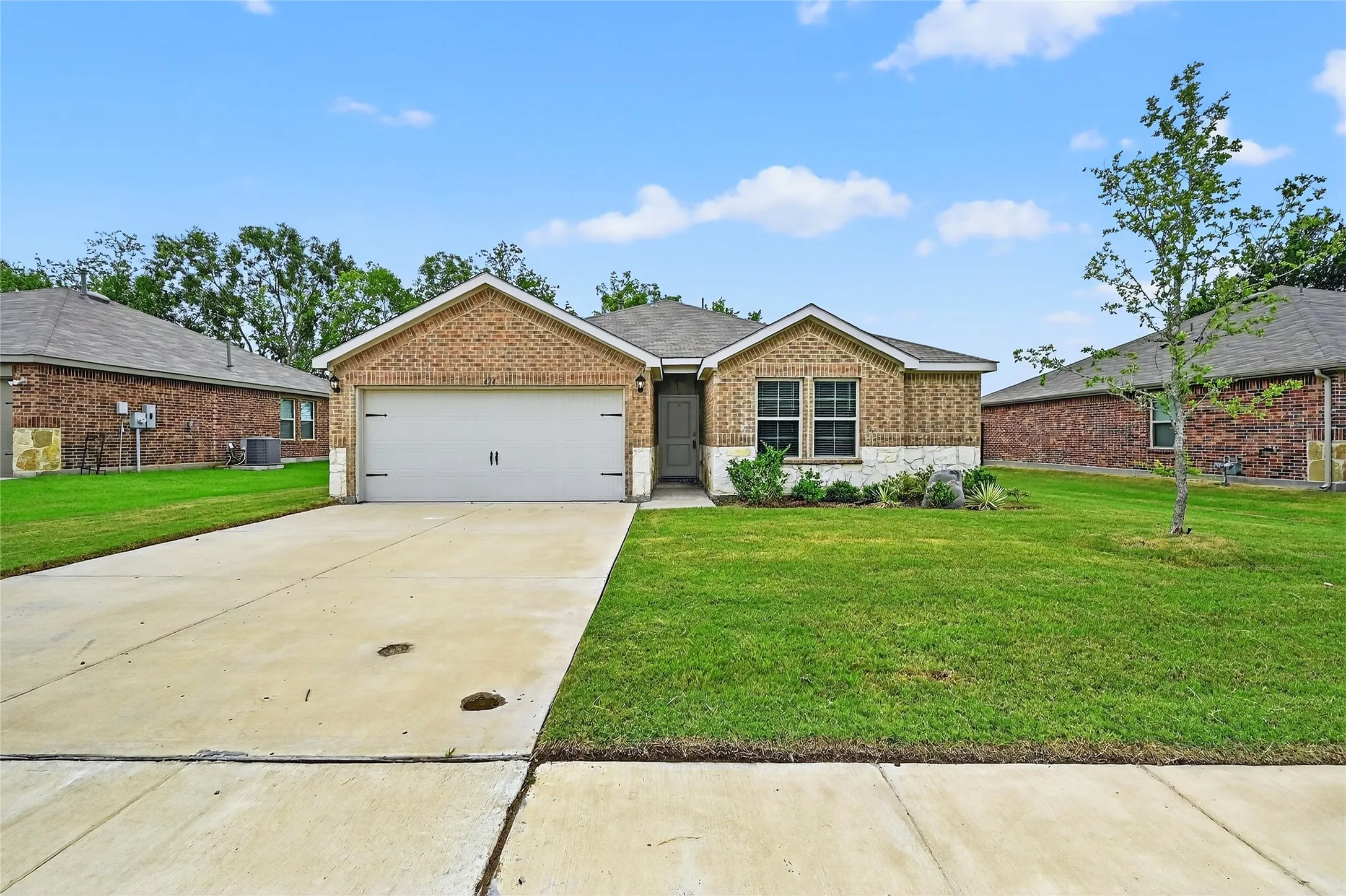 Ranch-style house with an attached garage, brick siding, concrete driveway, and a front yard