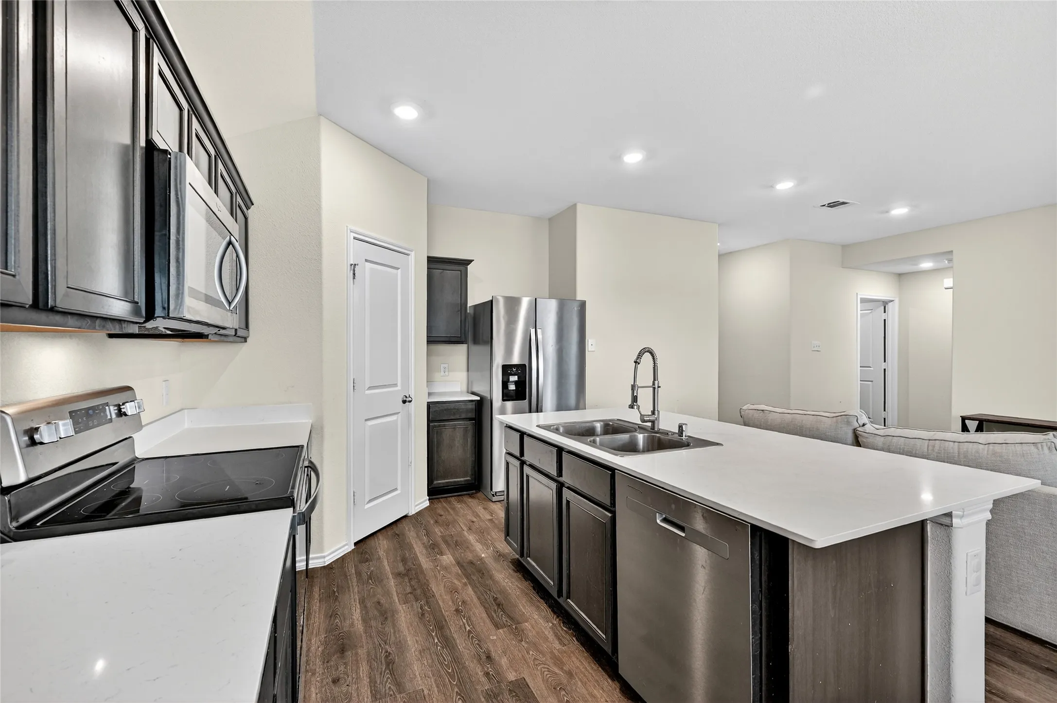 Kitchen featuring stainless steel appliances, dark wood-style floors, light countertops, recessed lighting, and a kitchen island with sink
