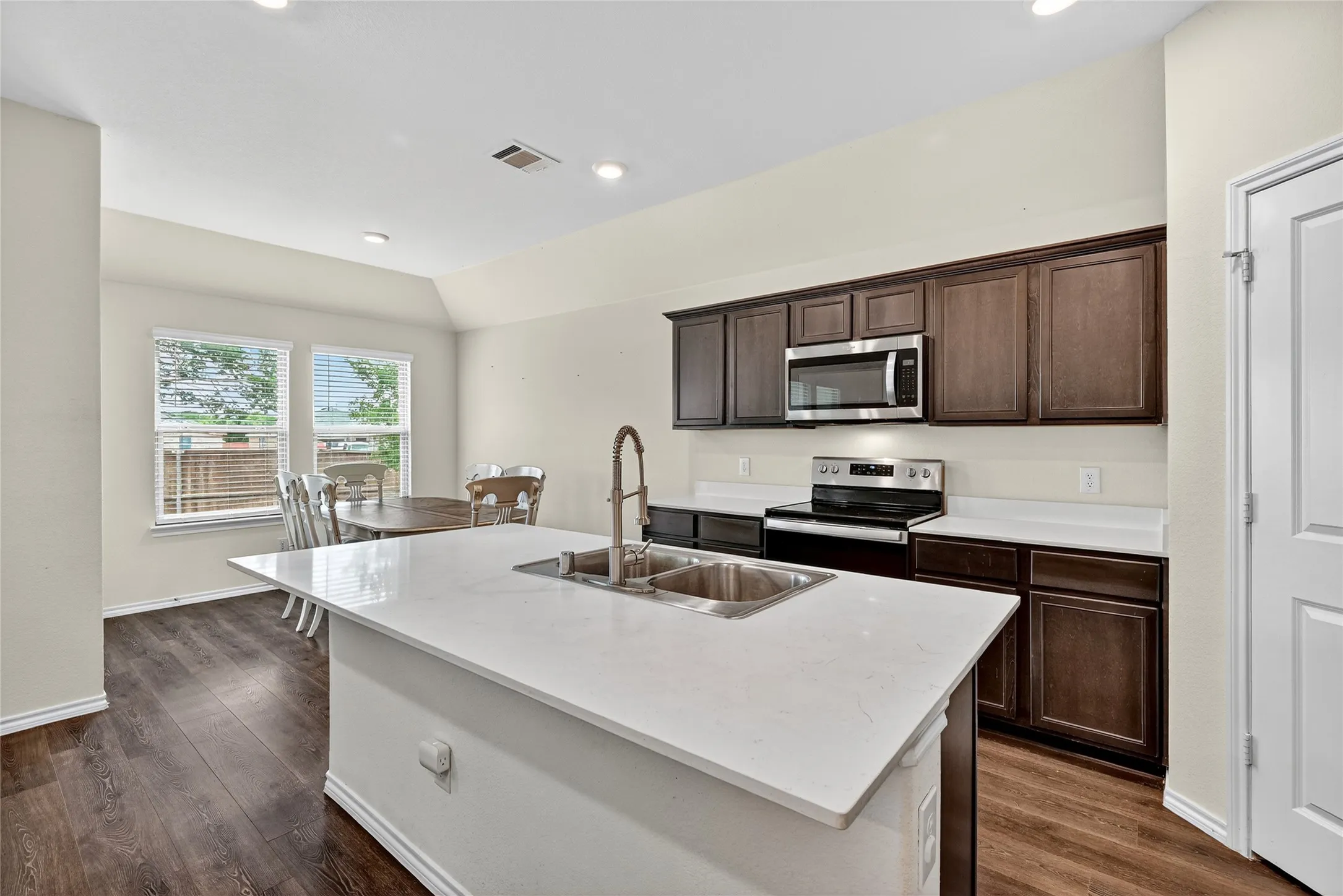 Kitchen featuring stainless steel appliances, a kitchen island with sink, dark wood-style floors, dark brown cabinets, and recessed lighting