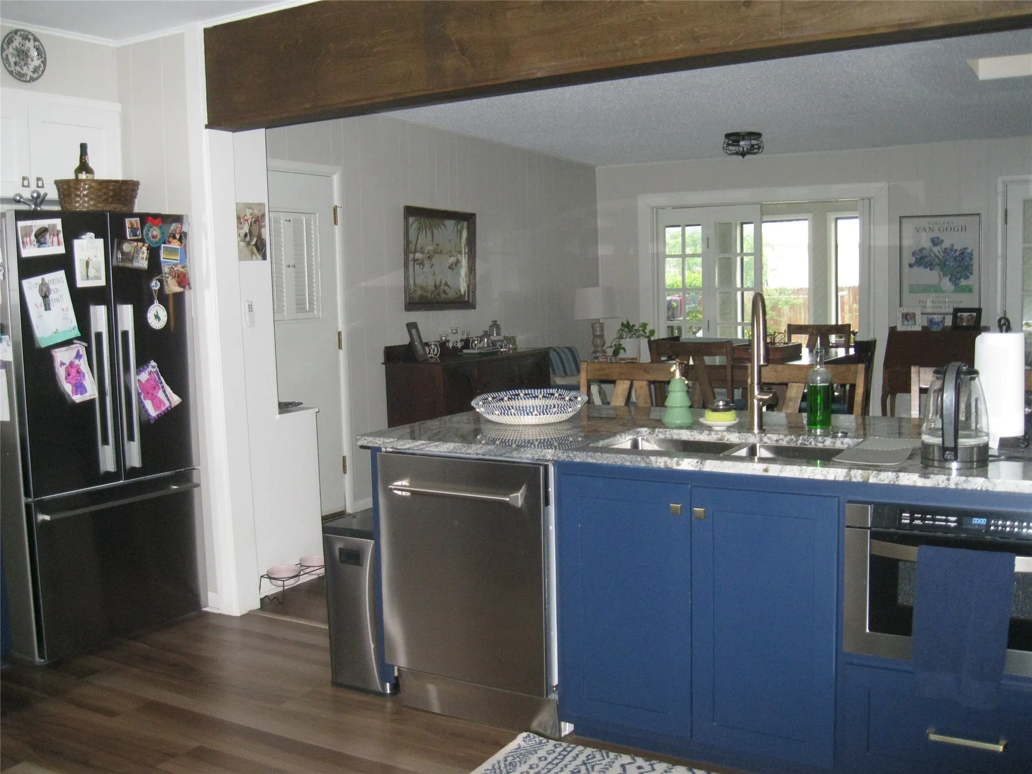 Kitchen with stainless steel appliances, blue cabinetry, light stone counters, and dark wood finished floors
