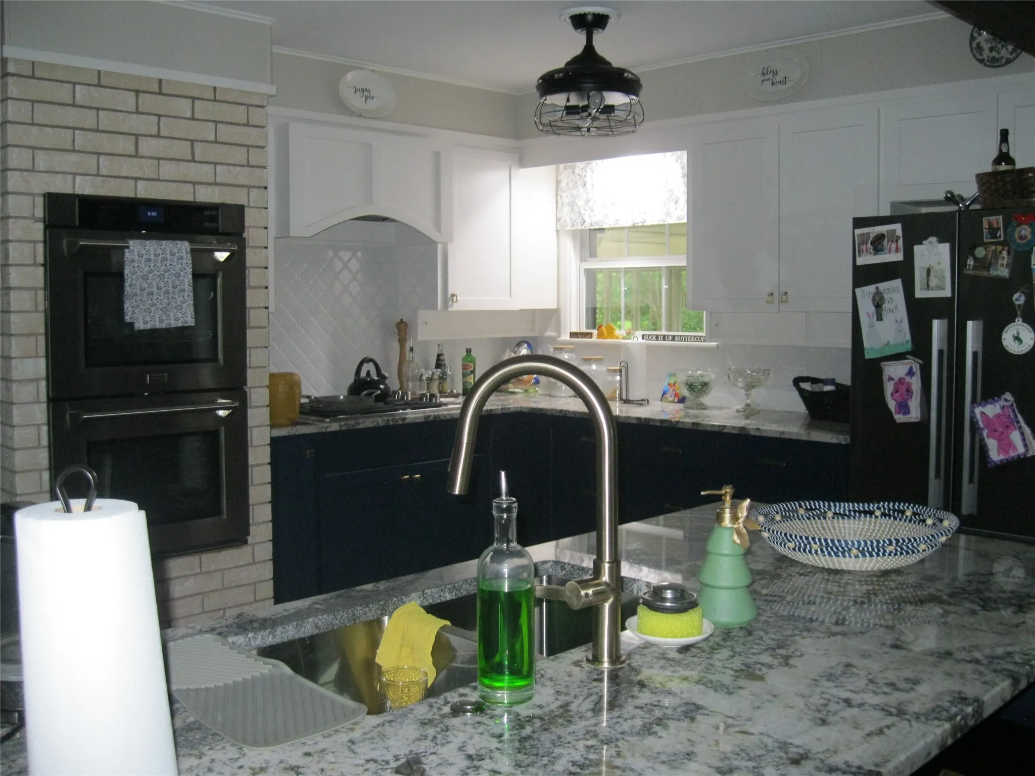 Kitchen with black appliances, light stone countertops, white cabinetry, crown molding, and tasteful backsplash