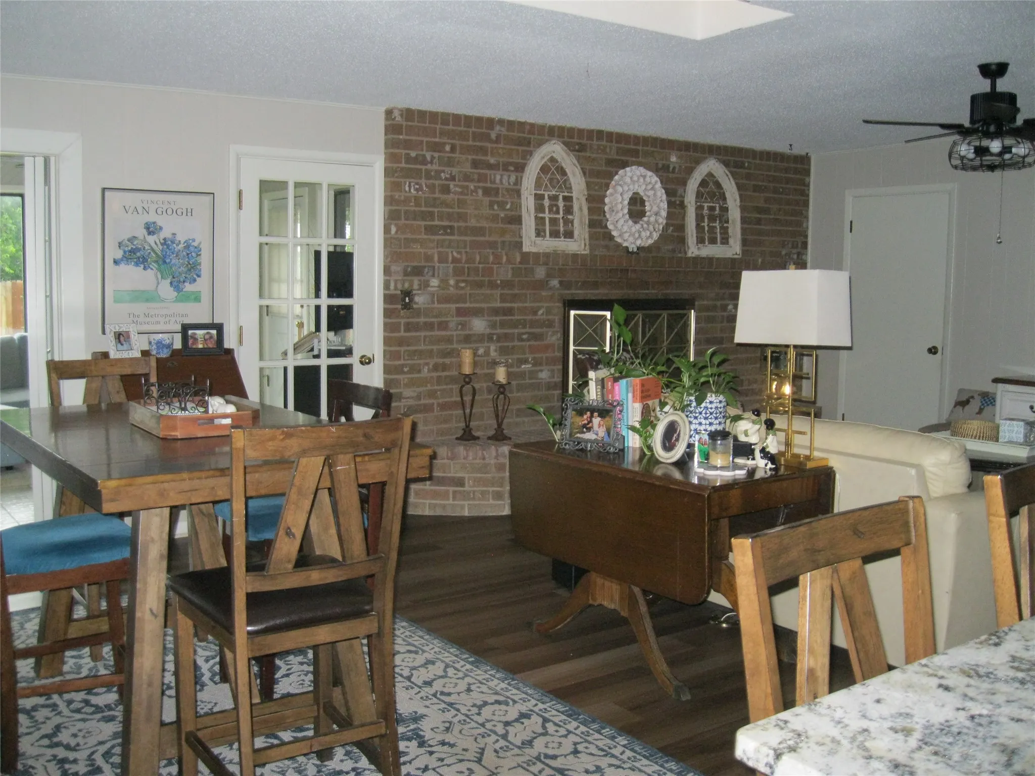 Dining room with wood finished floors, ceiling fan, a brick fireplace, a textured ceiling, and brick wall