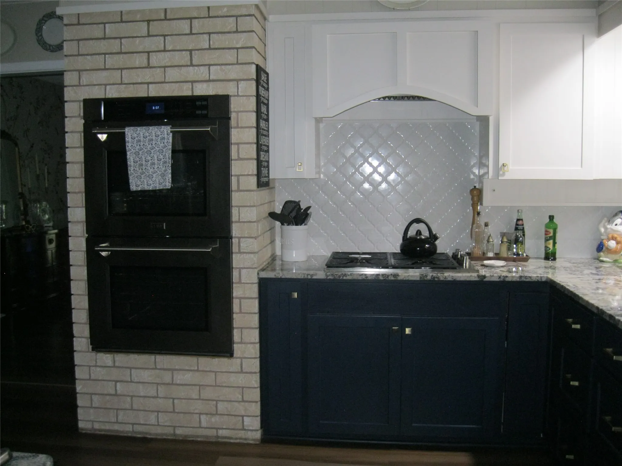 Kitchen with light stone counters, stainless steel gas cooktop, tasteful backsplash, white cabinetry, and dark cabinets