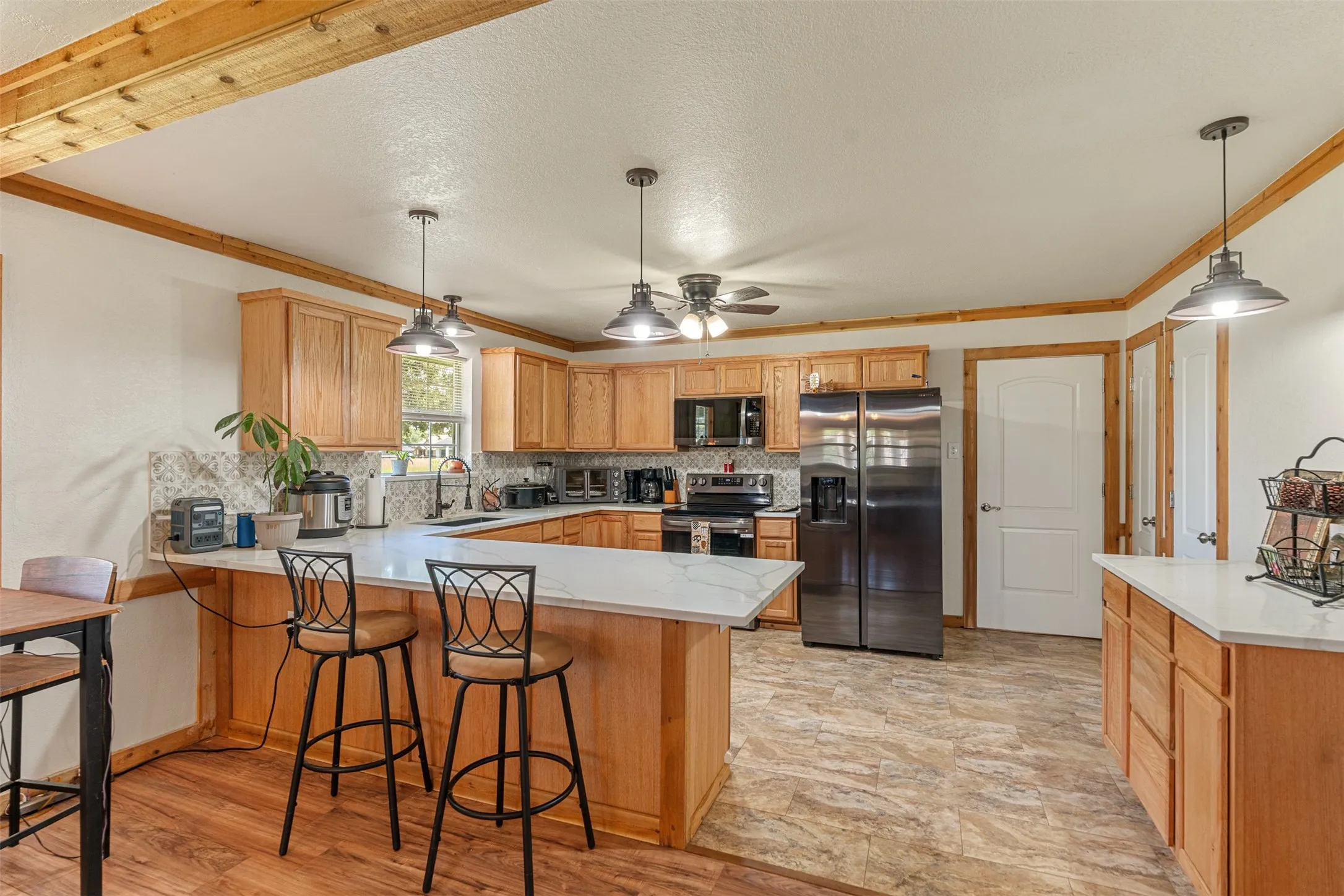 Kitchen featuring a peninsula, stainless steel appliances, decorative backsplash, ornamental molding, and a ceiling fan