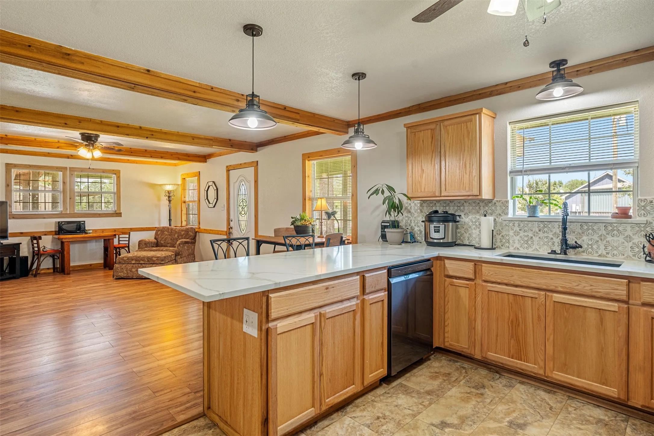 Kitchen with ceiling fan, a peninsula, dishwashing machine, plenty of natural light, and beamed ceiling