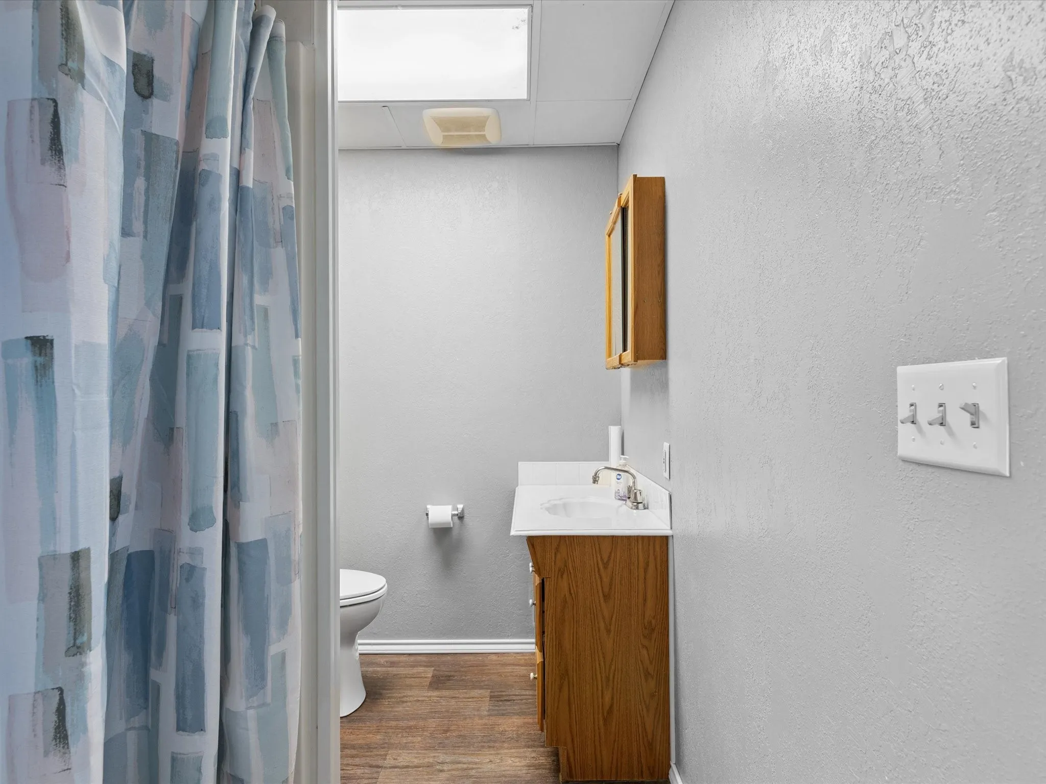 Bathroom with wood finished floors, vanity, a textured wall, a drop ceiling, and a shower with curtain