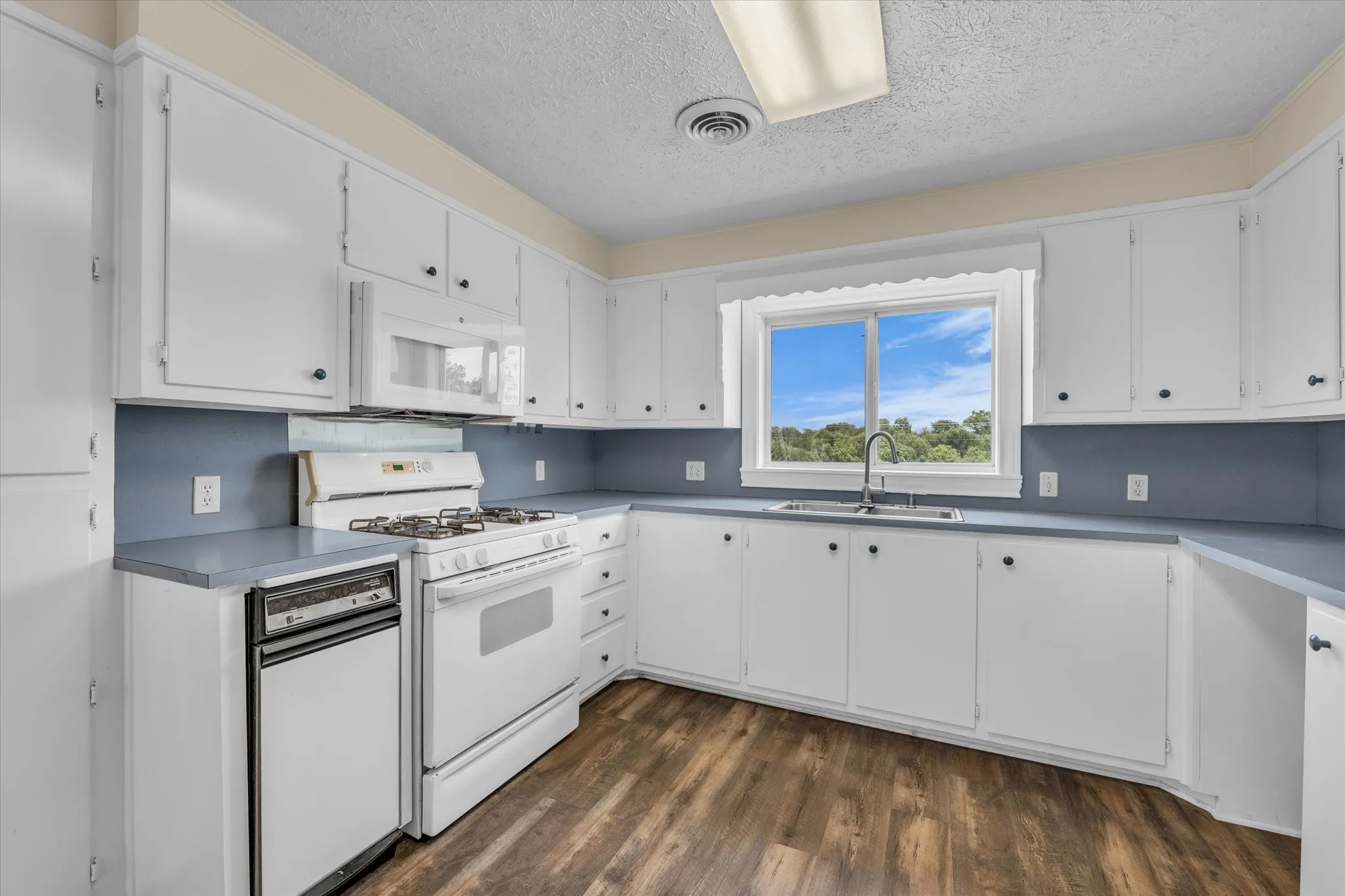 Kitchen with white appliances, a textured ceiling, dark wood-type flooring, and white cabinets