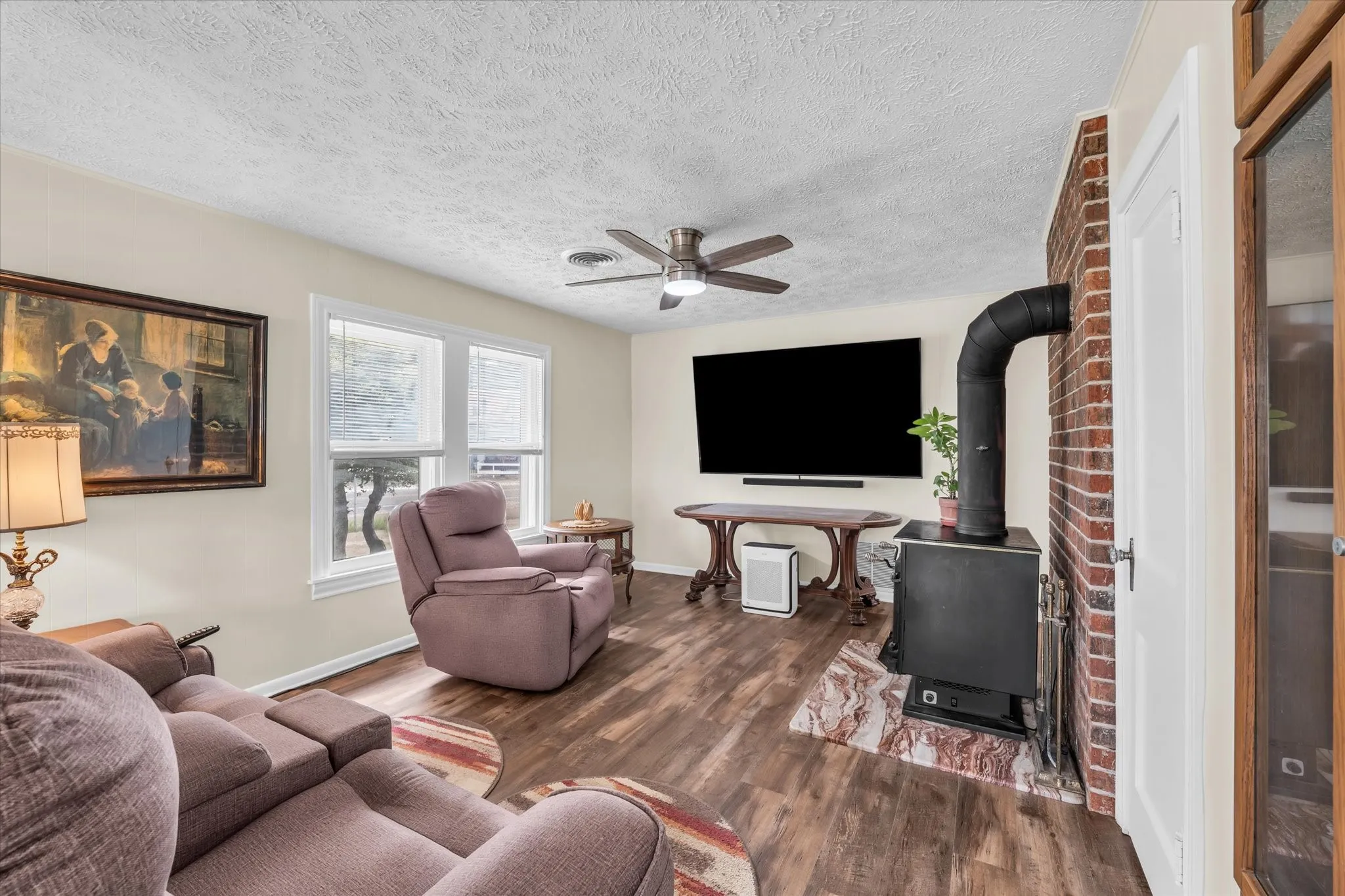 Living area with a wood stove, wood finished floors, a ceiling fan, and a textured ceiling