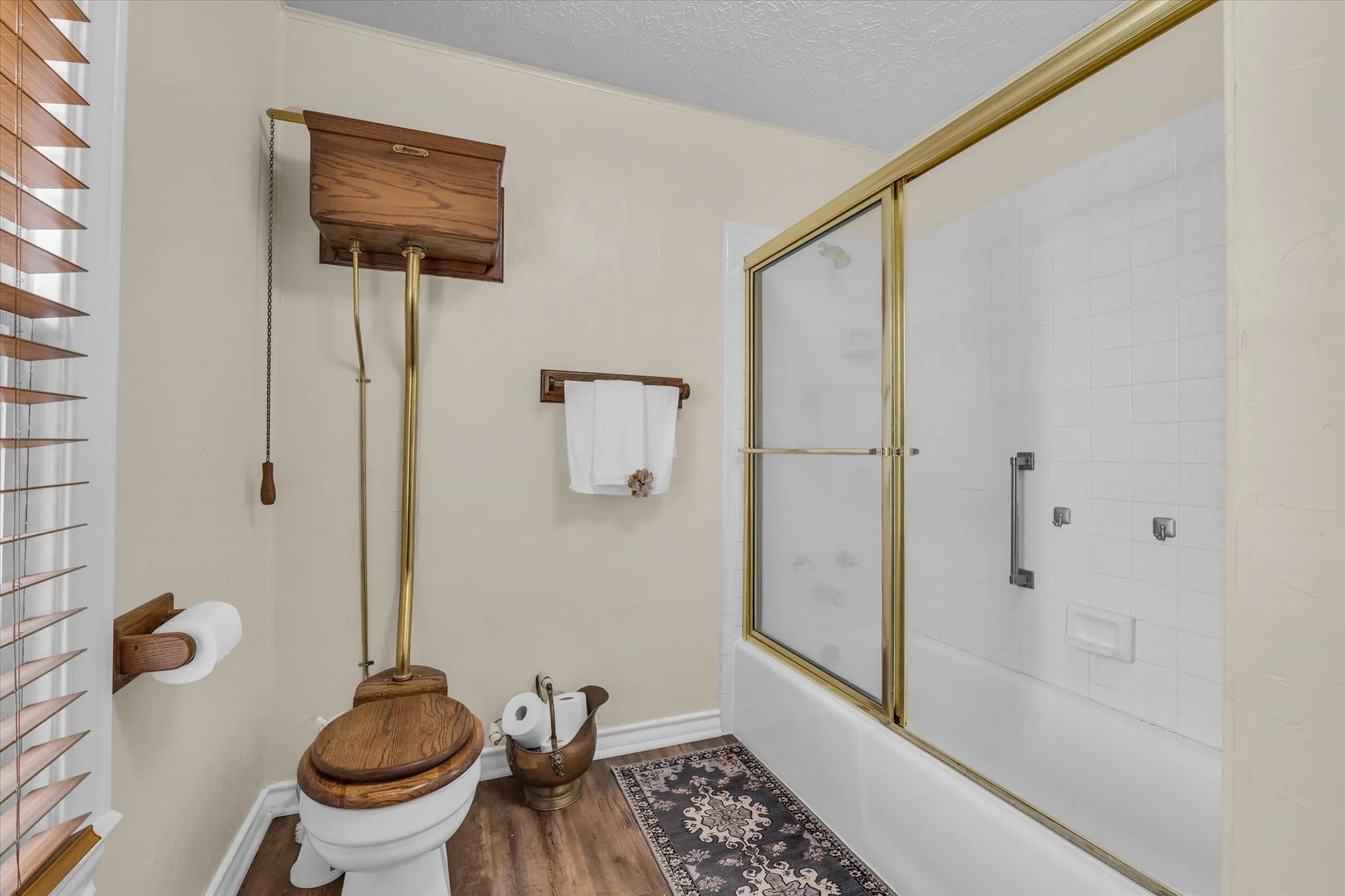 Bathroom featuring bath / shower combo with glass door, wood finished floors, and a textured ceiling