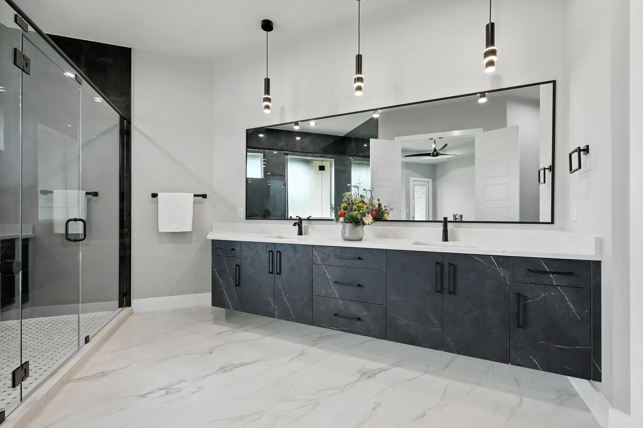 Full bath featuring a ceiling fan, double vanity, marble tiled floors, and a shower stall