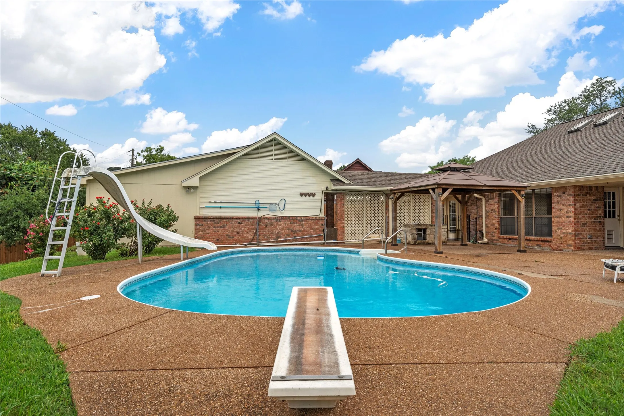 View of pool with a water slide, a gazebo, a diving board, and a patio area