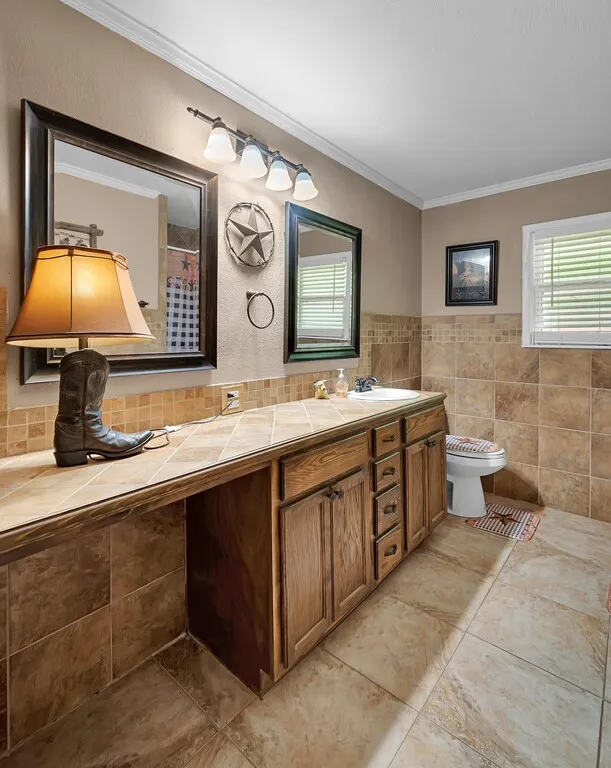 Bathroom featuring tile patterned flooring, ornamental molding, double vanity, tile walls, and a shower with curtain