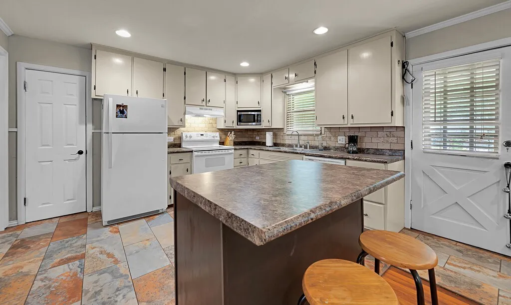 Kitchen featuring white appliances, under cabinet range hood, dark countertops, tasteful backsplash, and crown molding