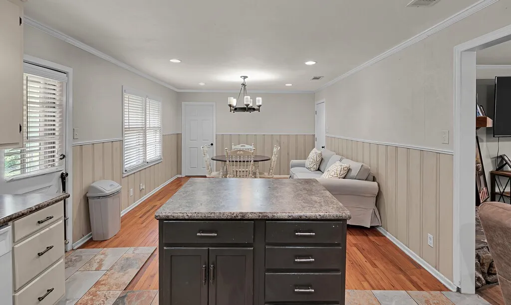 Kitchen featuring a wainscoted wall, light wood-type flooring, a chandelier, dark cabinets, and a kitchen island
