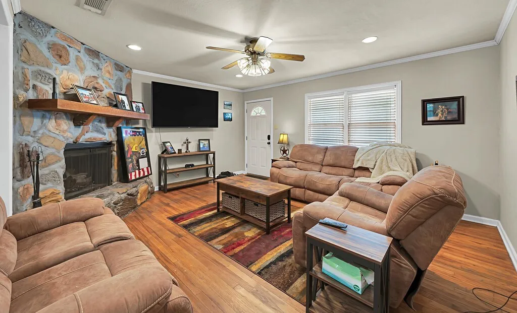 Living room with a ceiling fan, crown molding, recessed lighting, wood-type flooring, and a stone fireplace