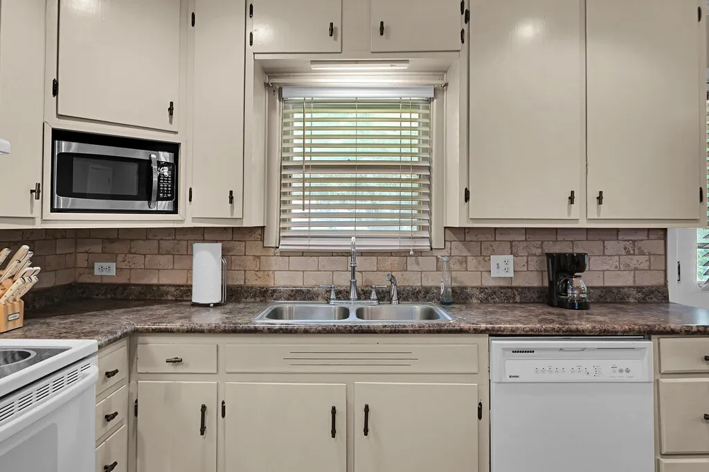 Kitchen with white appliances, dark countertops, tasteful backsplash, and white cabinetry