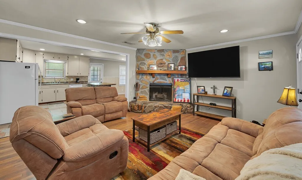 Living room with ornamental molding, ceiling fan, light wood-style floors, recessed lighting, and a stone fireplace