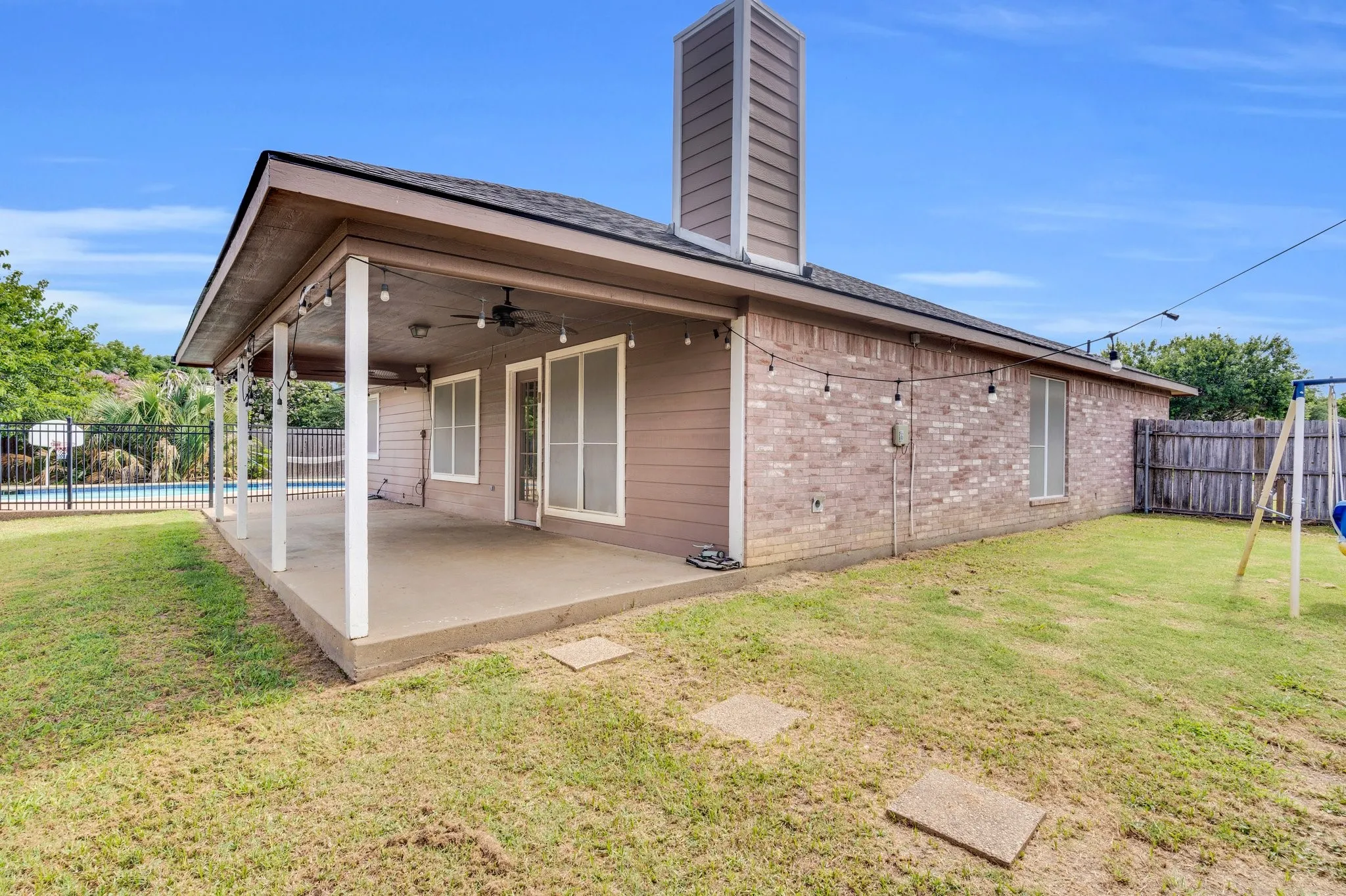 Rear view of house with brick siding, a chimney, a fenced backyard, a patio, and ceiling fan