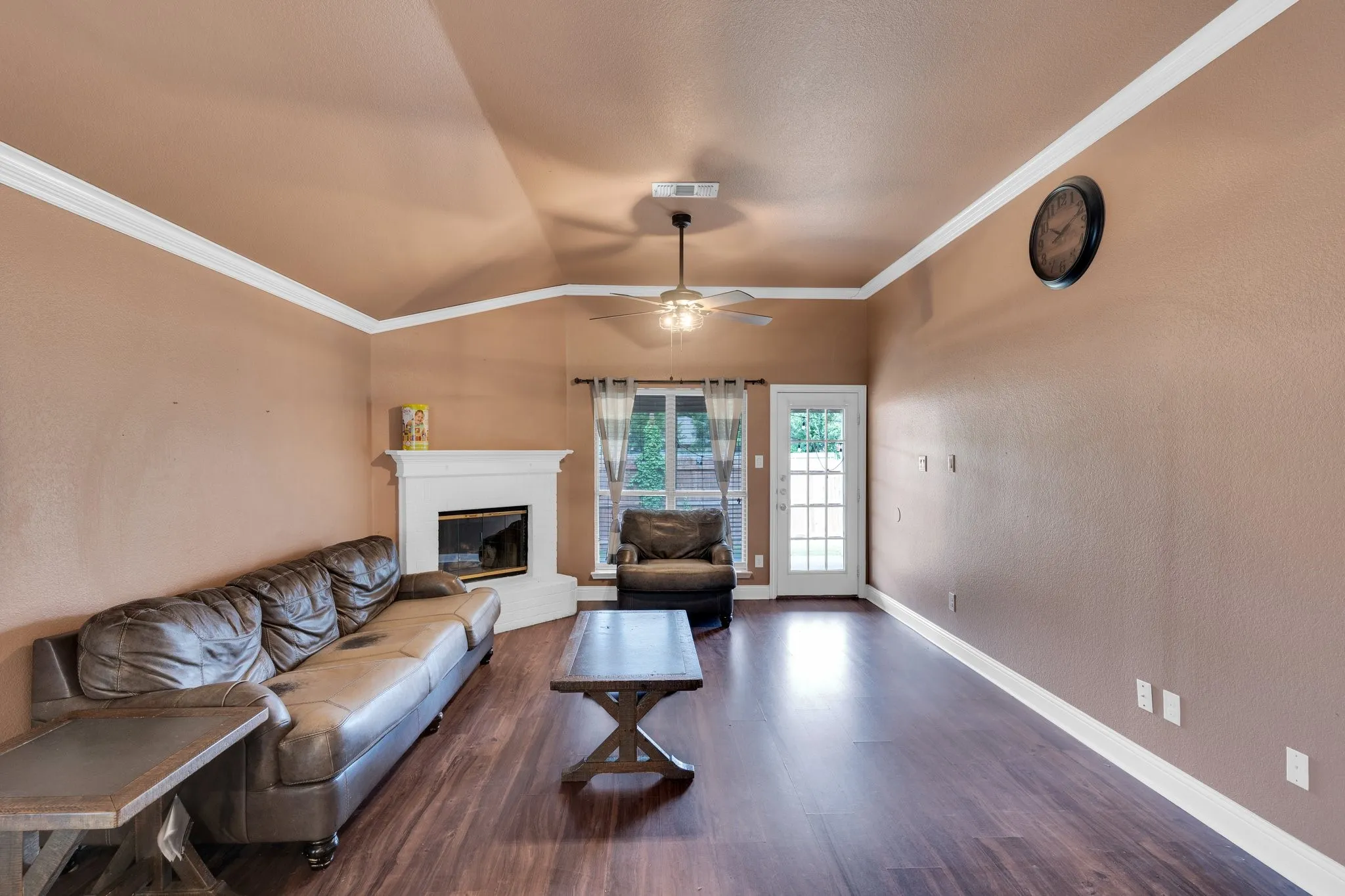 Living room with lofted ceiling, ornamental molding, a glass covered fireplace, dark wood finished floors, and a ceiling fan