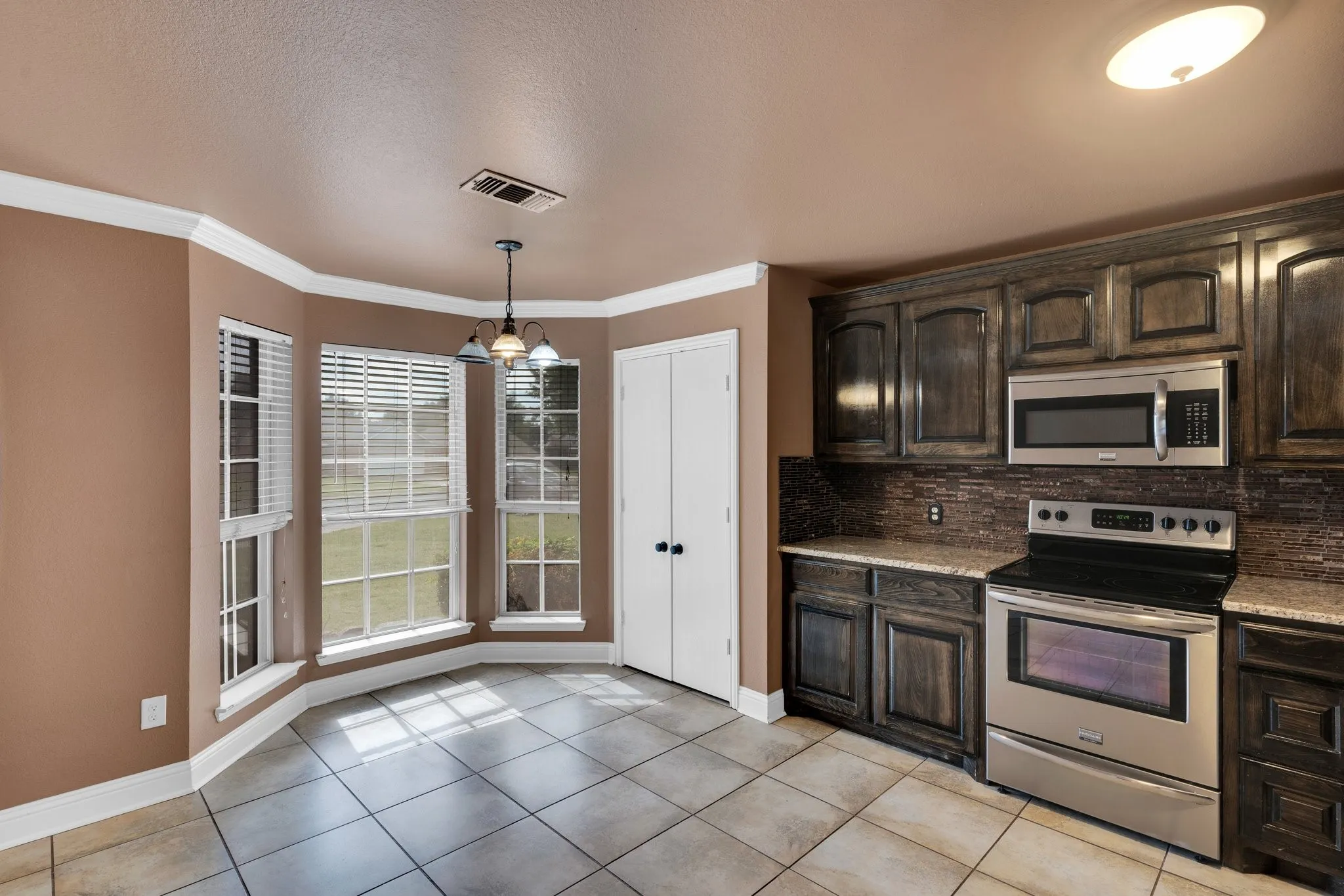 Kitchen with stainless steel appliances, tasteful backsplash, light tile patterned floors, dark brown cabinetry, and hanging light fixtures