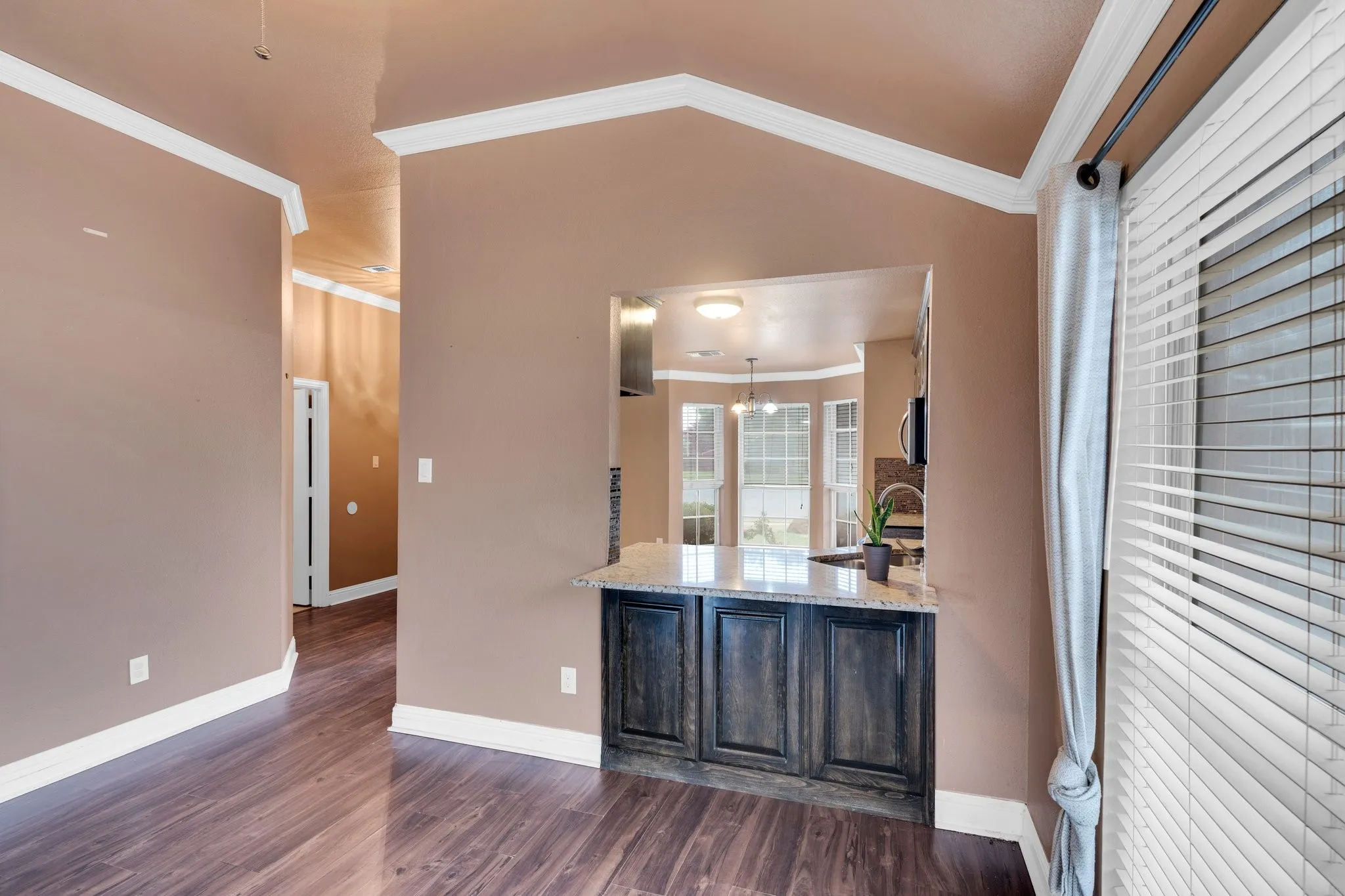 Kitchen with ornamental molding, dark wood finished floors, stainless steel microwave, light stone counters, and lofted ceiling