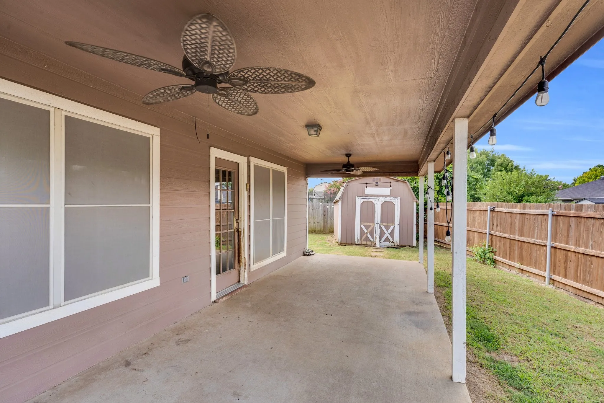Fenced backyard with ceiling fan, a patio, and a storage unit