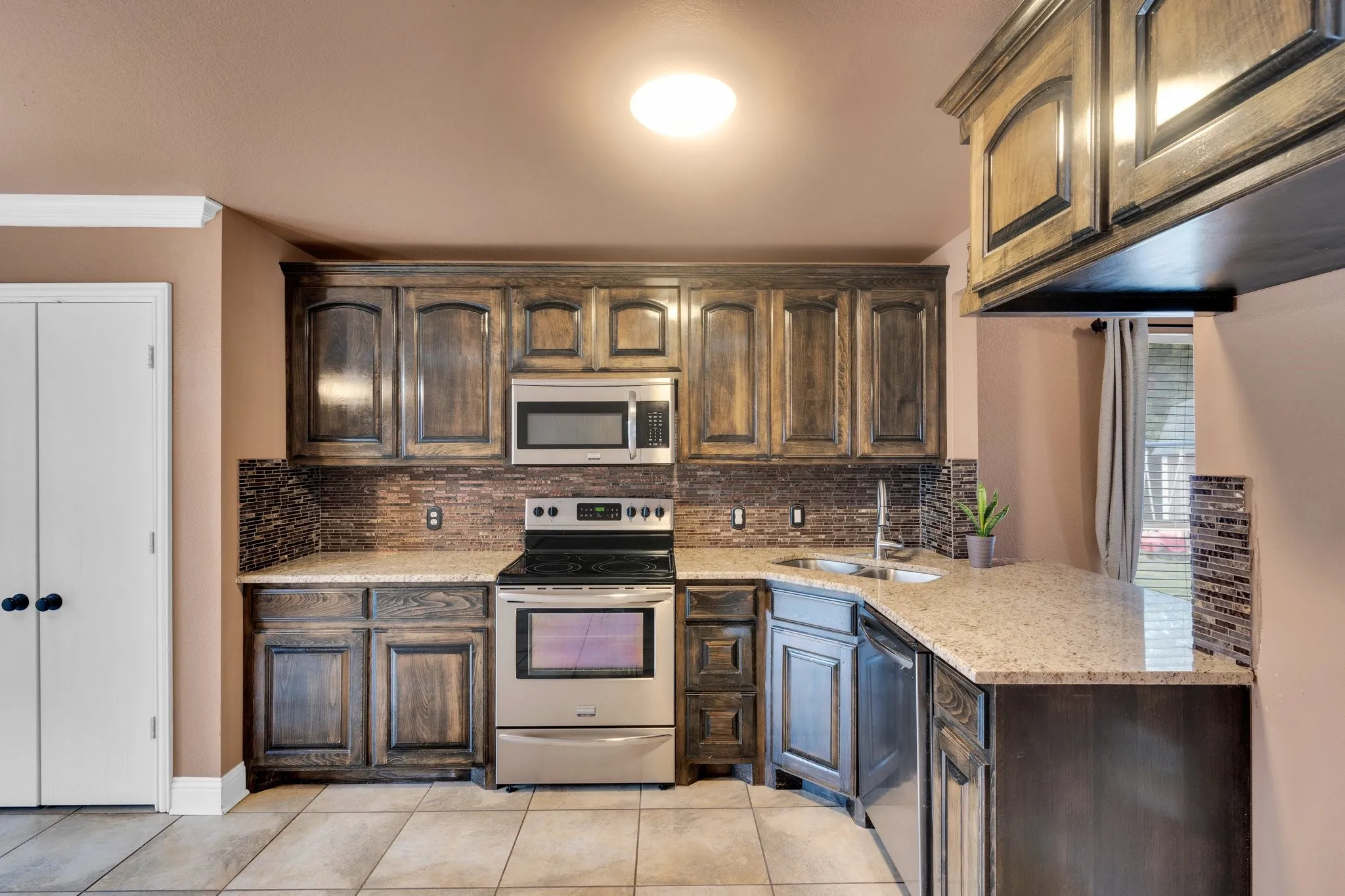 Kitchen featuring appliances with stainless steel finishes, decorative backsplash, light tile patterned floors, light stone countertops, and crown molding