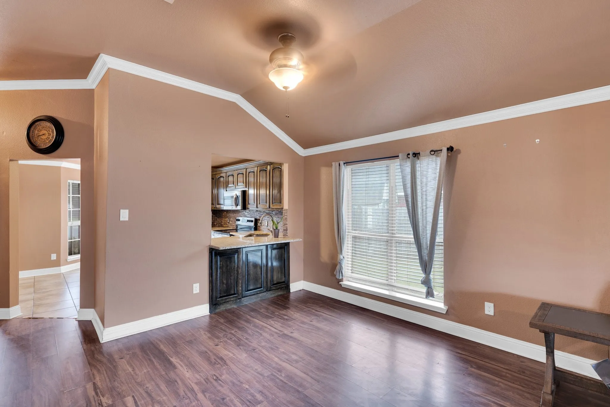 Unfurnished living room featuring lofted ceiling, dark wood-style flooring, ornamental molding, and a ceiling fan