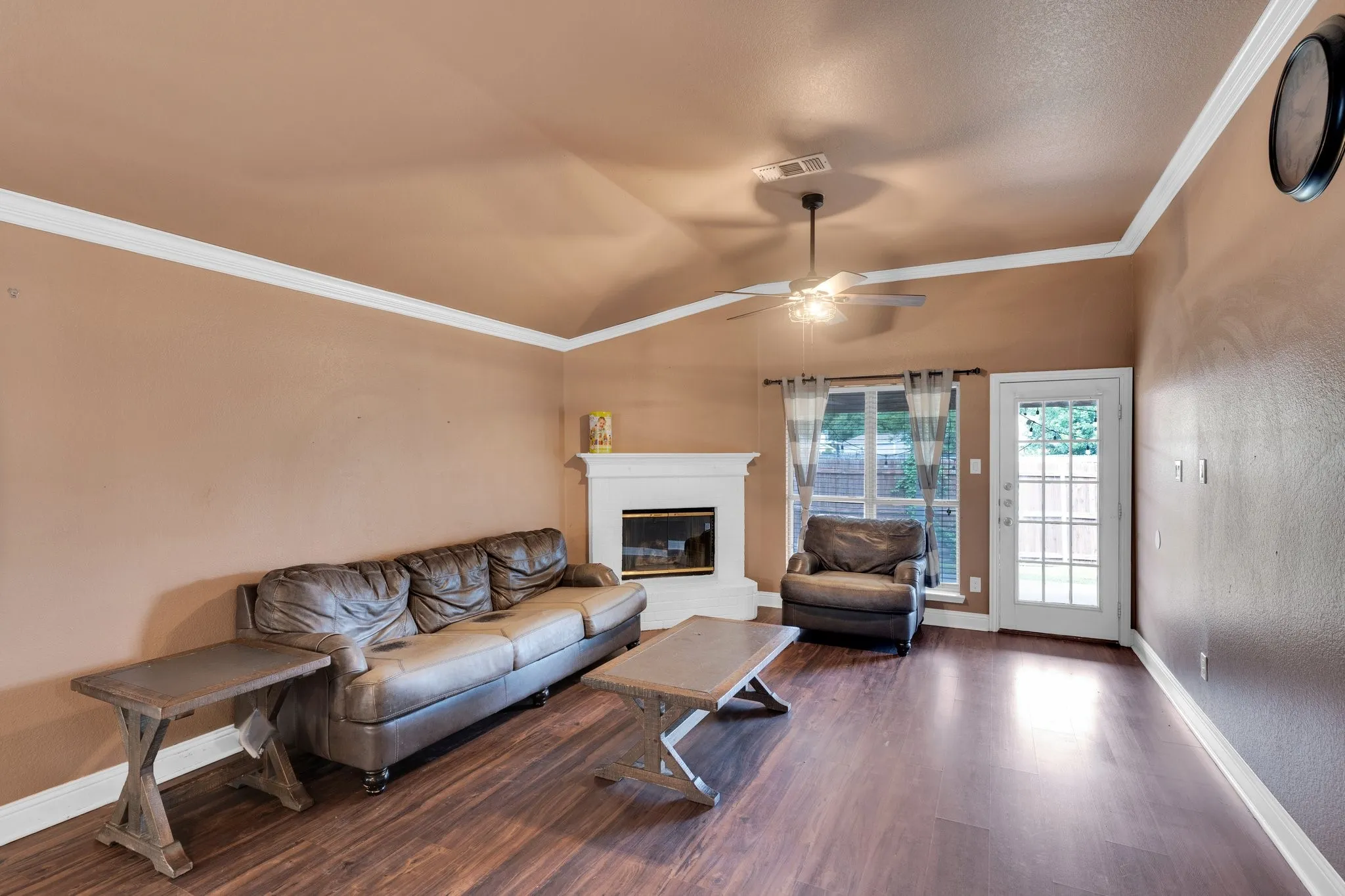 Living area featuring wood finished floors, a fireplace, ceiling fan, and crown molding