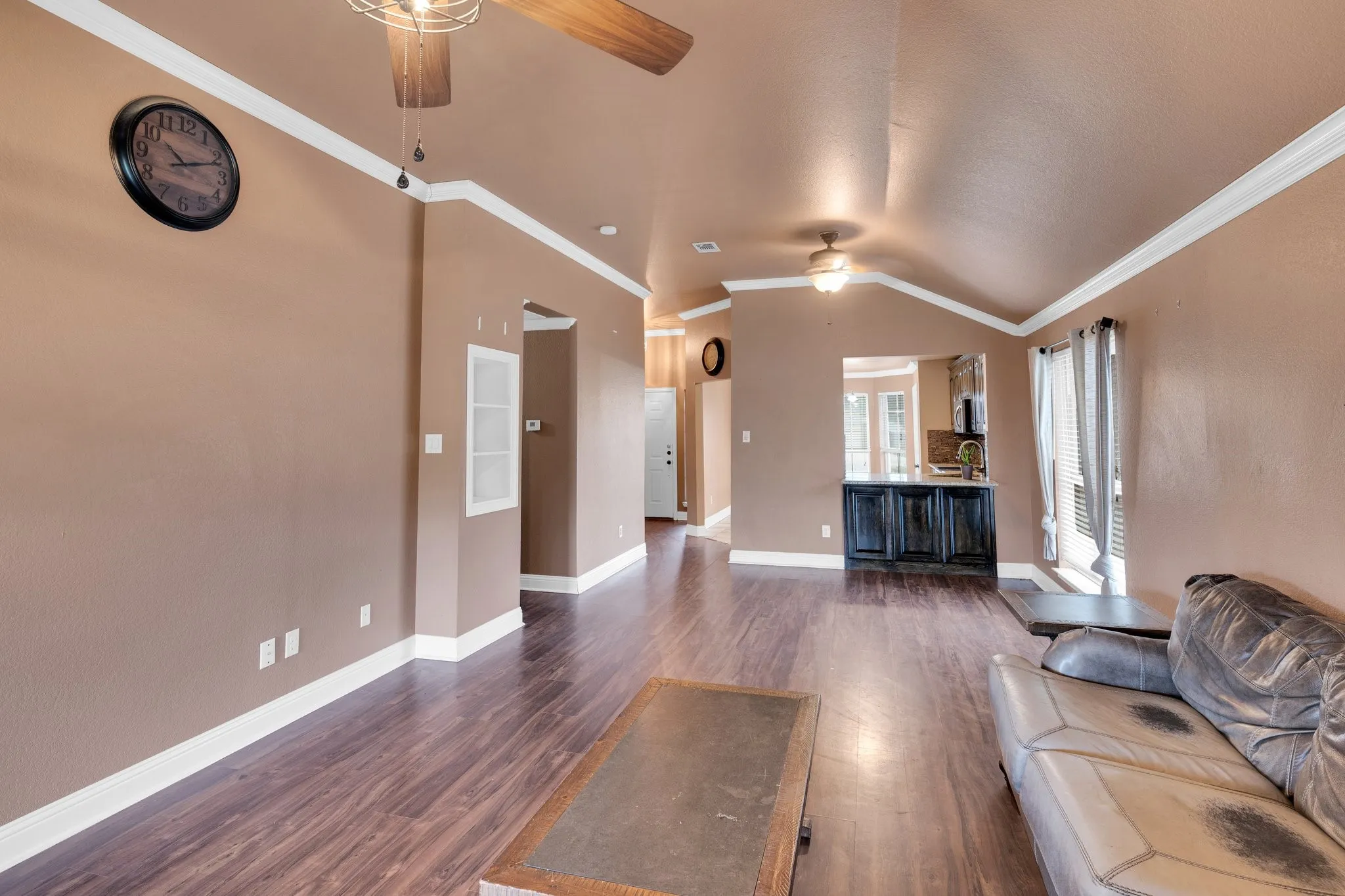 Living room with a ceiling fan, vaulted ceiling, crown molding, and dark wood finished floors