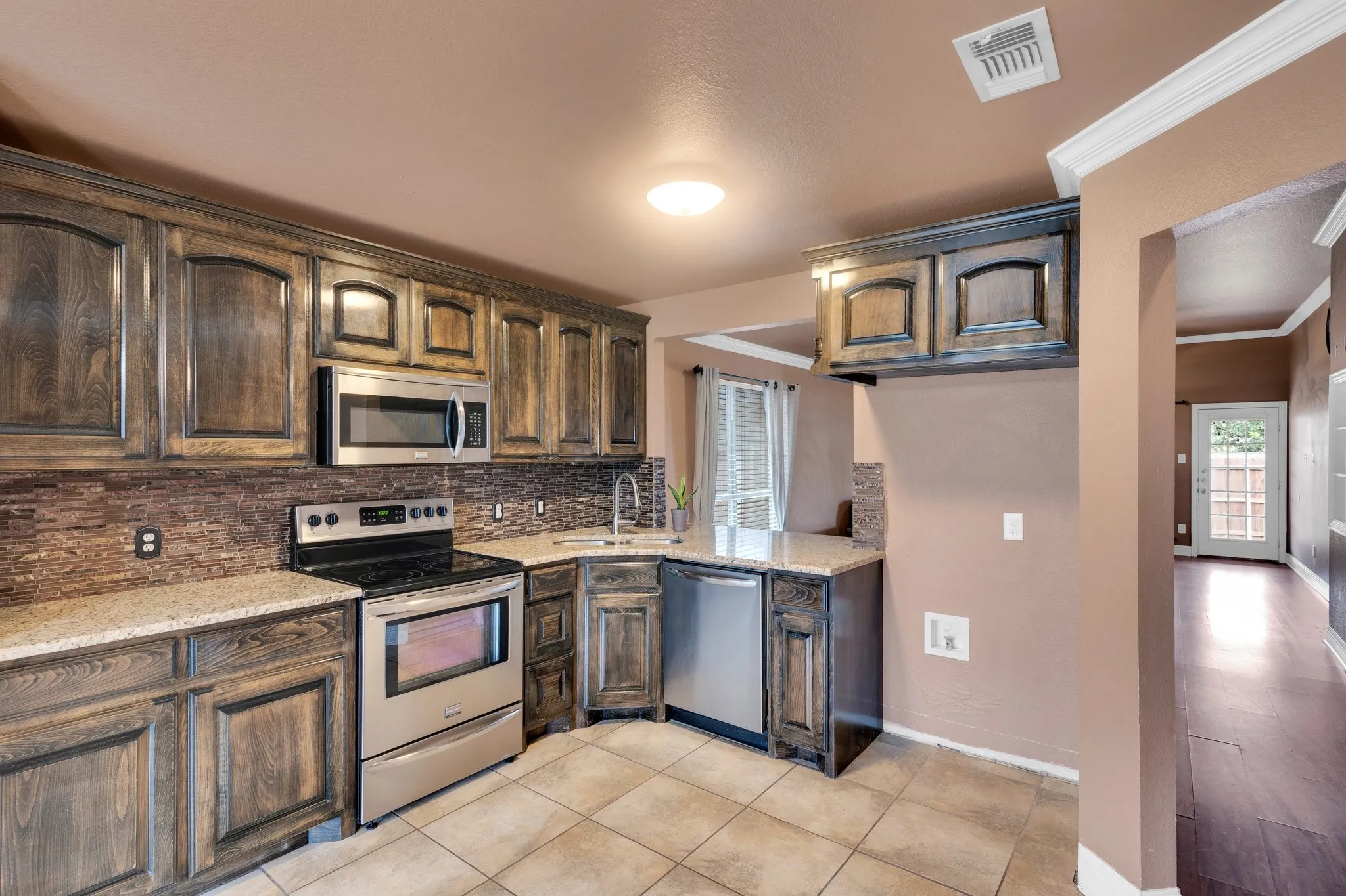 Kitchen with stainless steel appliances, decorative backsplash, light stone counters, ornamental molding, and dark brown cabinets