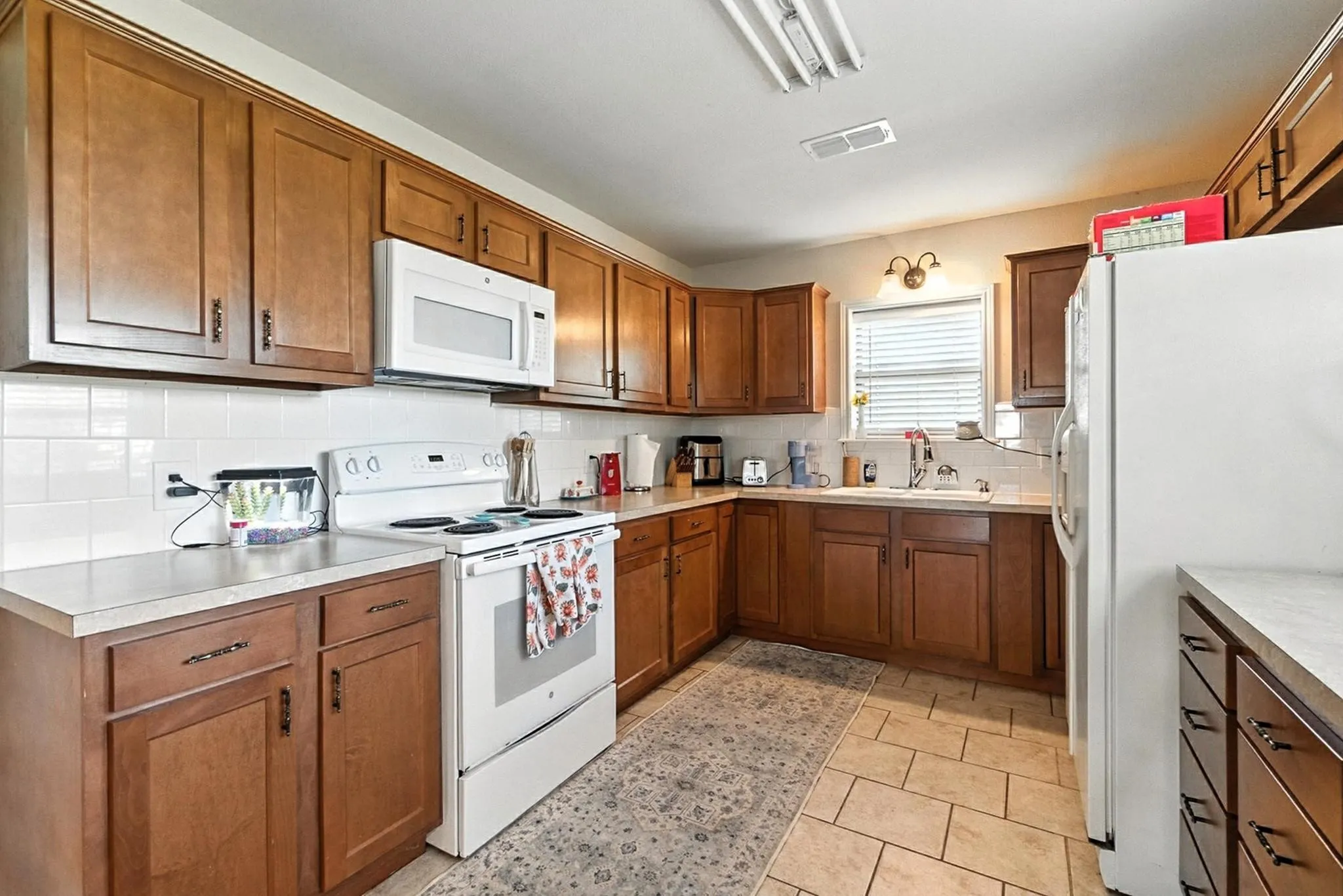 Kitchen featuring white appliances, brown cabinets, tasteful backsplash, and light countertops
