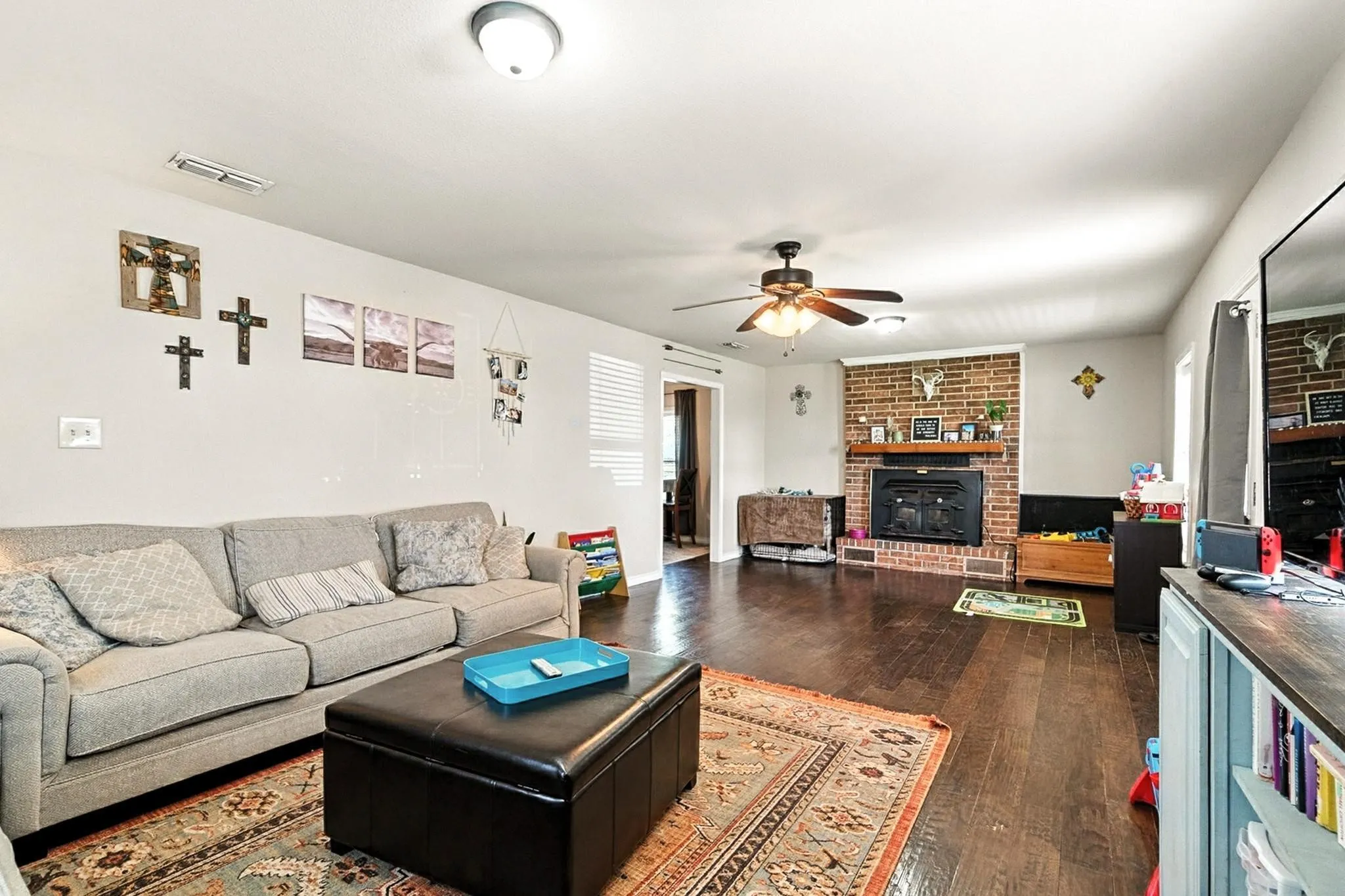 Living room with a ceiling fan, dark wood-style floors, and a fireplace