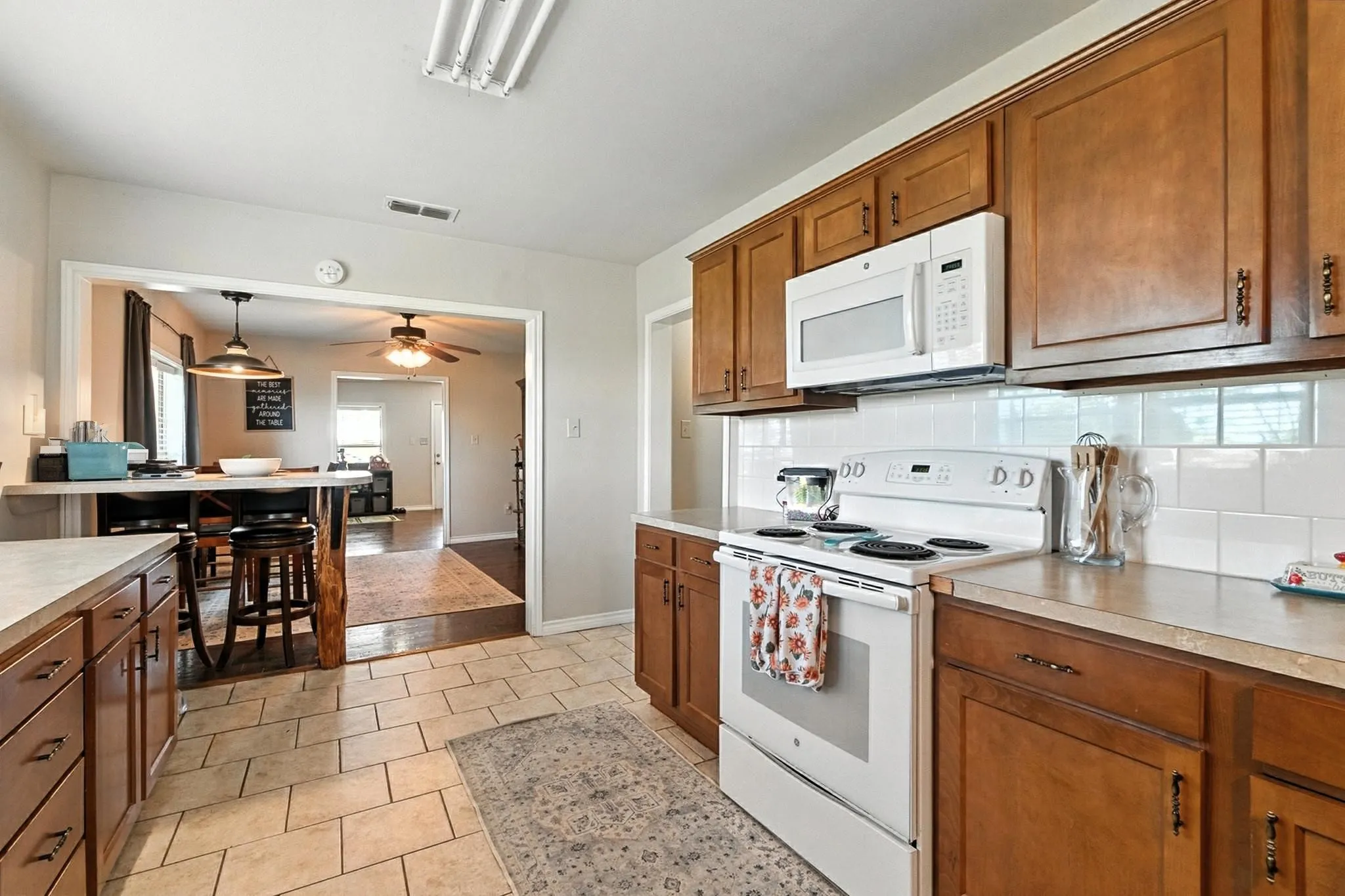 Kitchen featuring white appliances, brown cabinetry, decorative backsplash, a ceiling fan, and light countertops